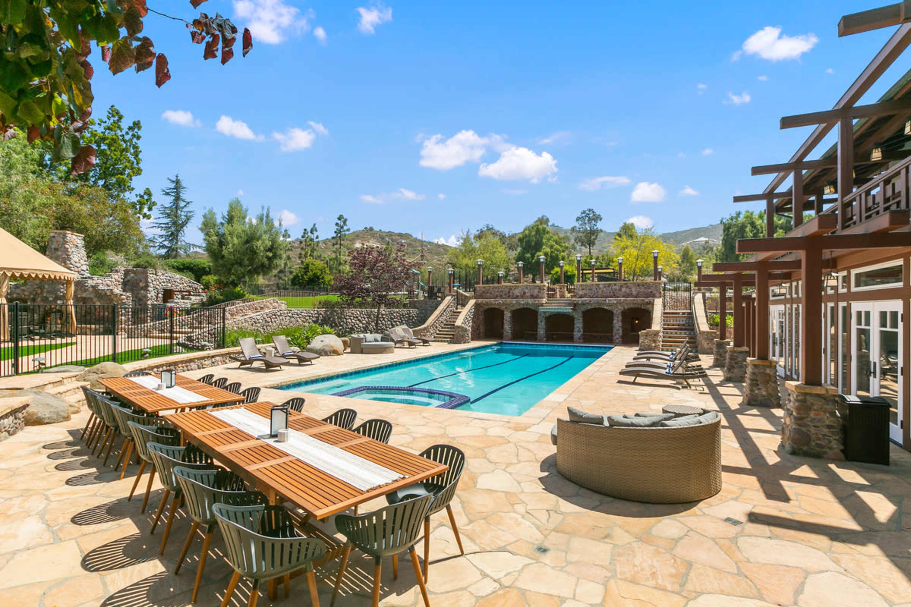 A spacious outdoor area features a swimming pool surrounded by lounge chairs and a long dining table.