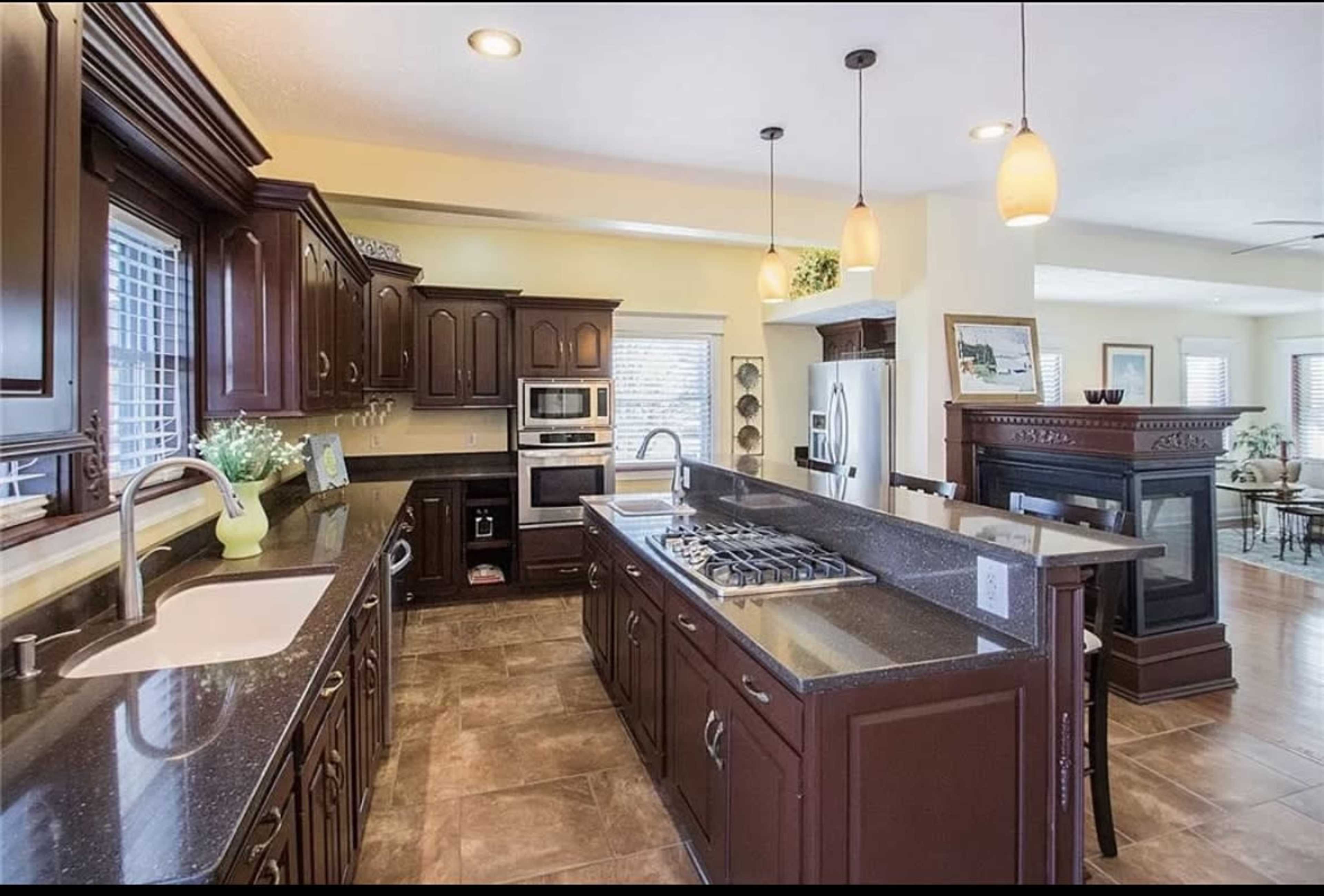 A spacious kitchen featuring dark wooden cabinets, stainless steel appliances, and a large countertop with a gas stove.