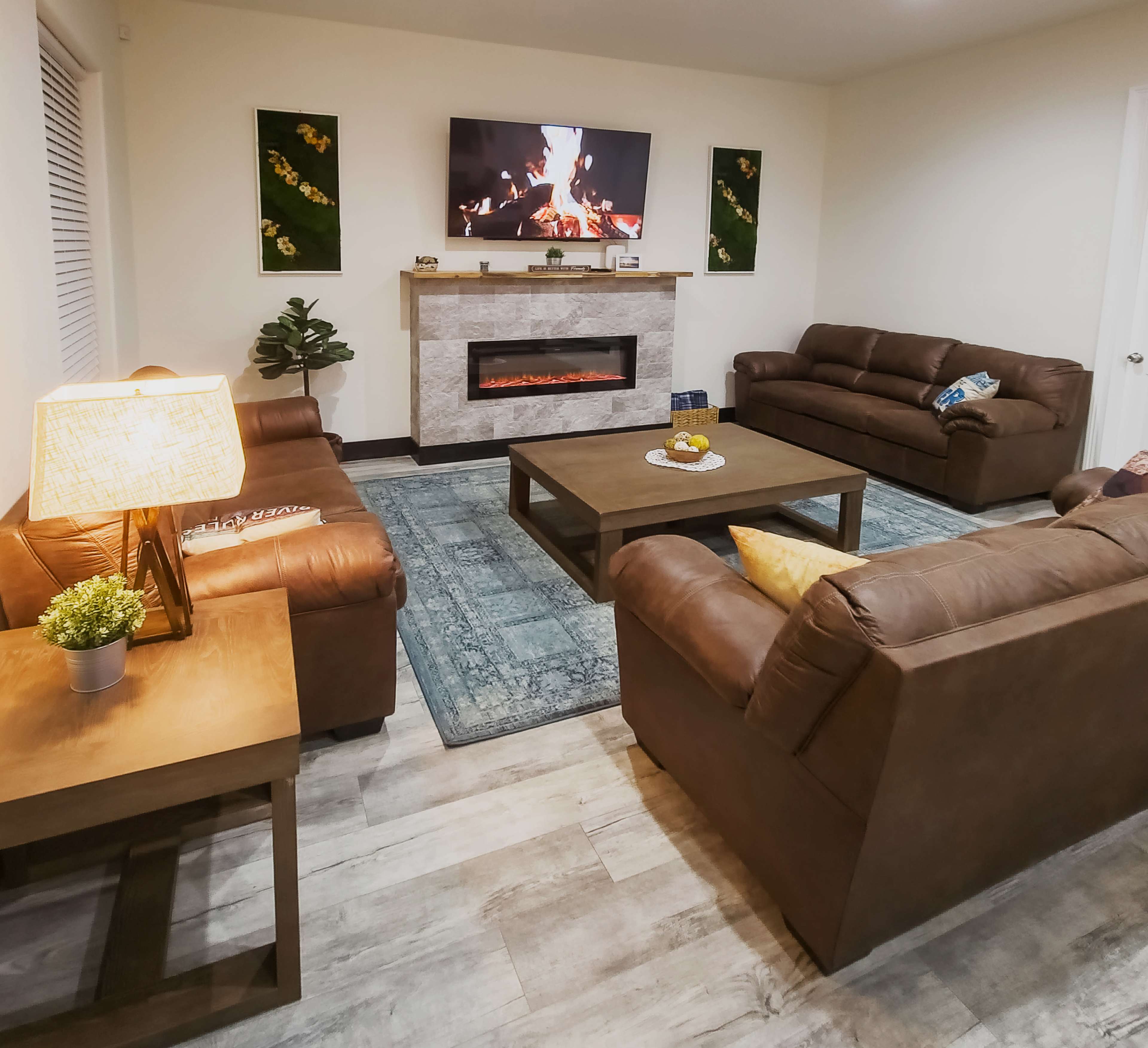 The living room features two brown leather sofas facing a coffee table, with a fireplace and a television mounted on the wall.