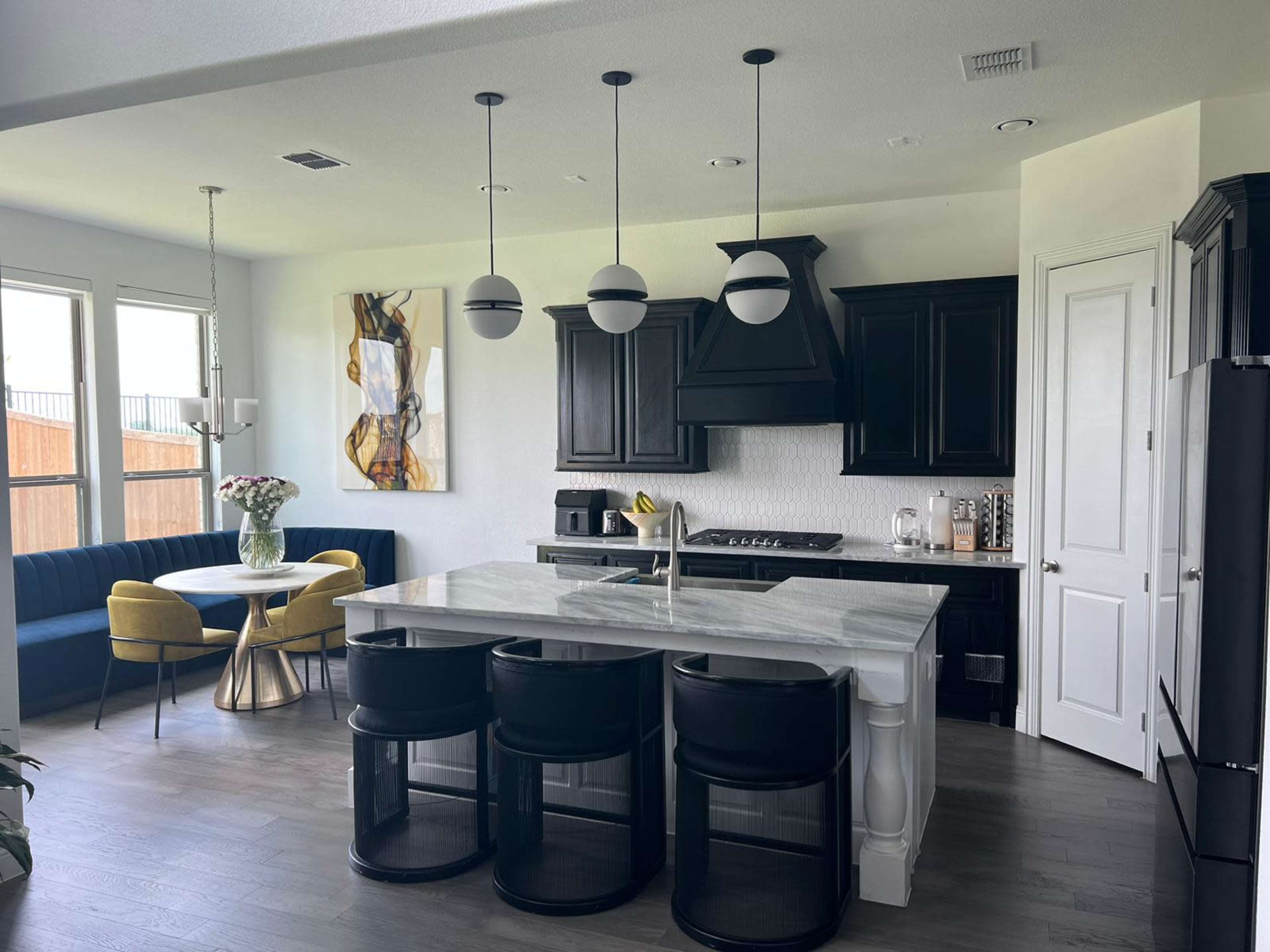 A modern kitchen with black cabinetry, a marble island, and a dining area featuring a circular table and yellow chairs.