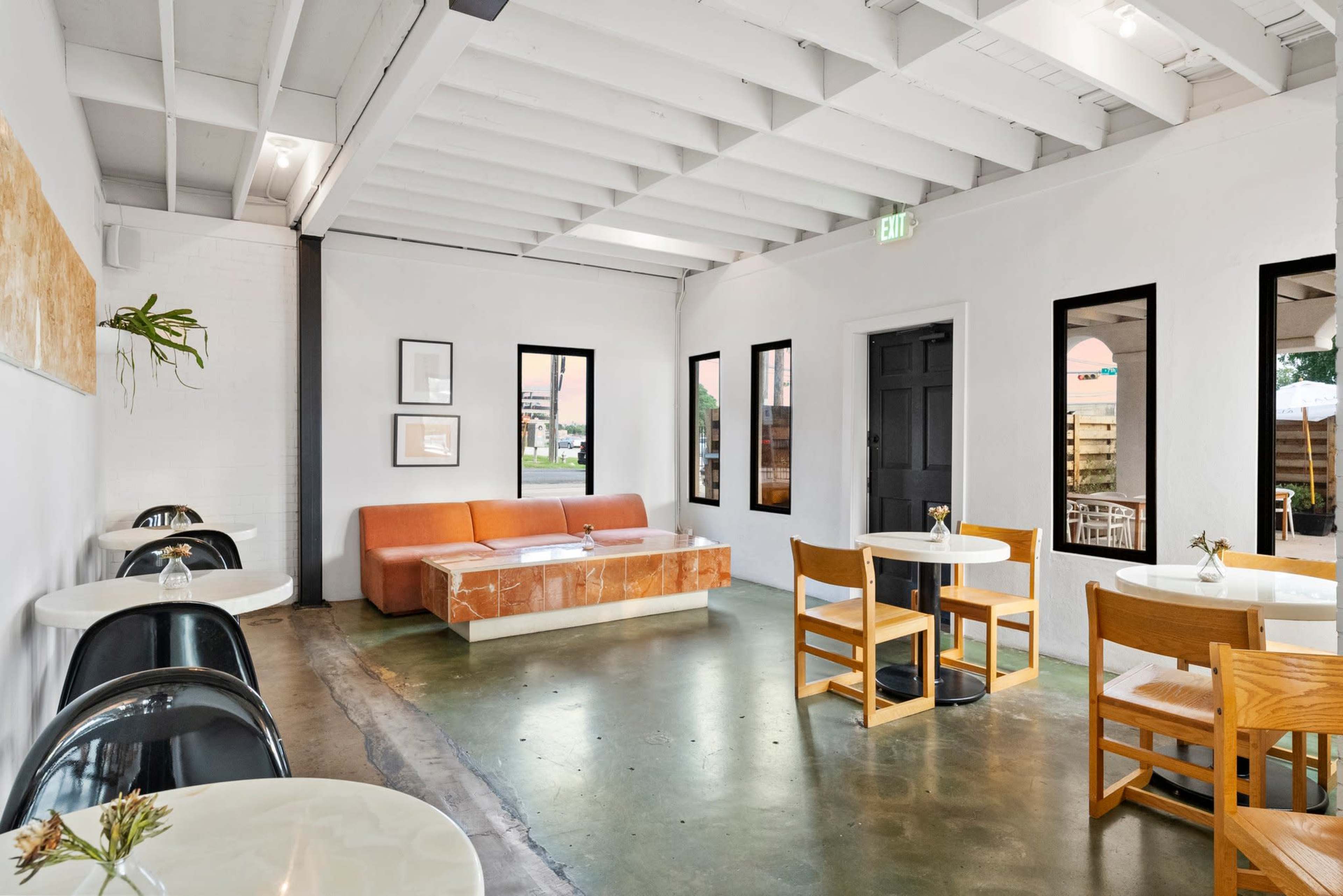 The image shows a modern cafe interior with white walls, wooden furniture, and a large orange couch.
