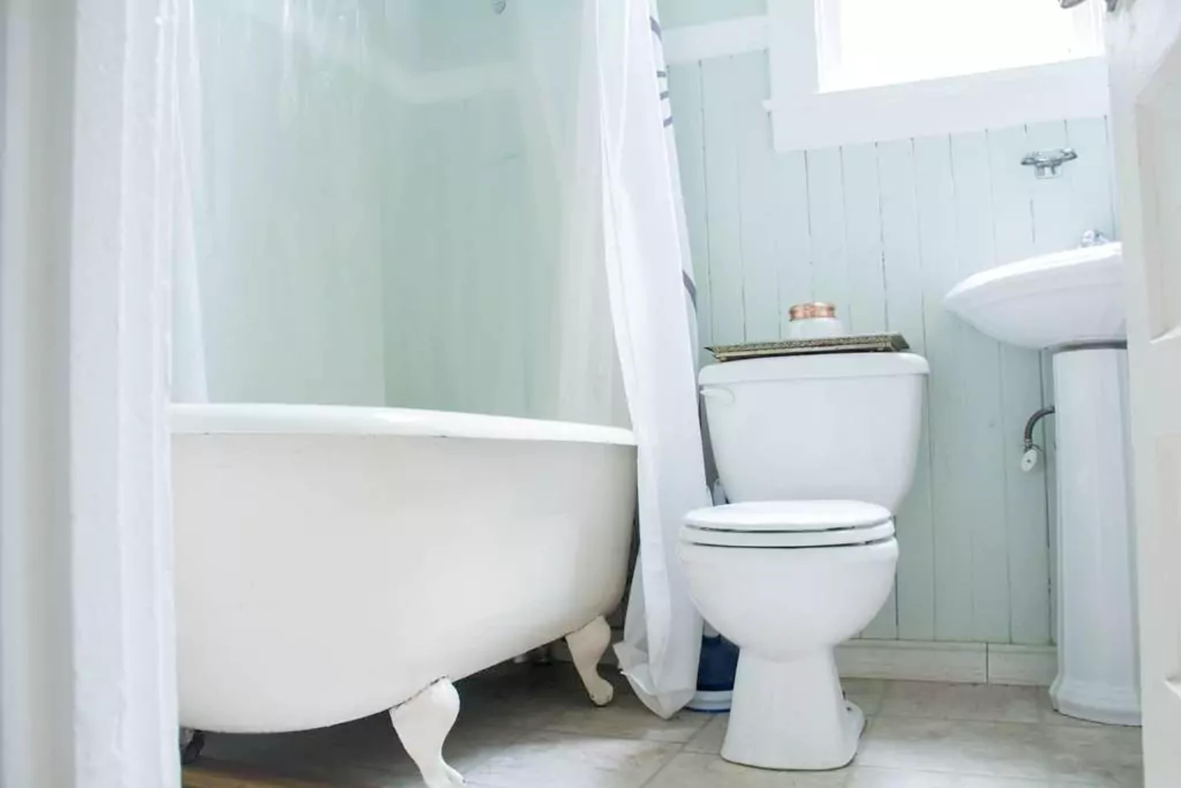 A white bathtub is positioned next to a toilet in a light-colored bathroom with pale green walls.
