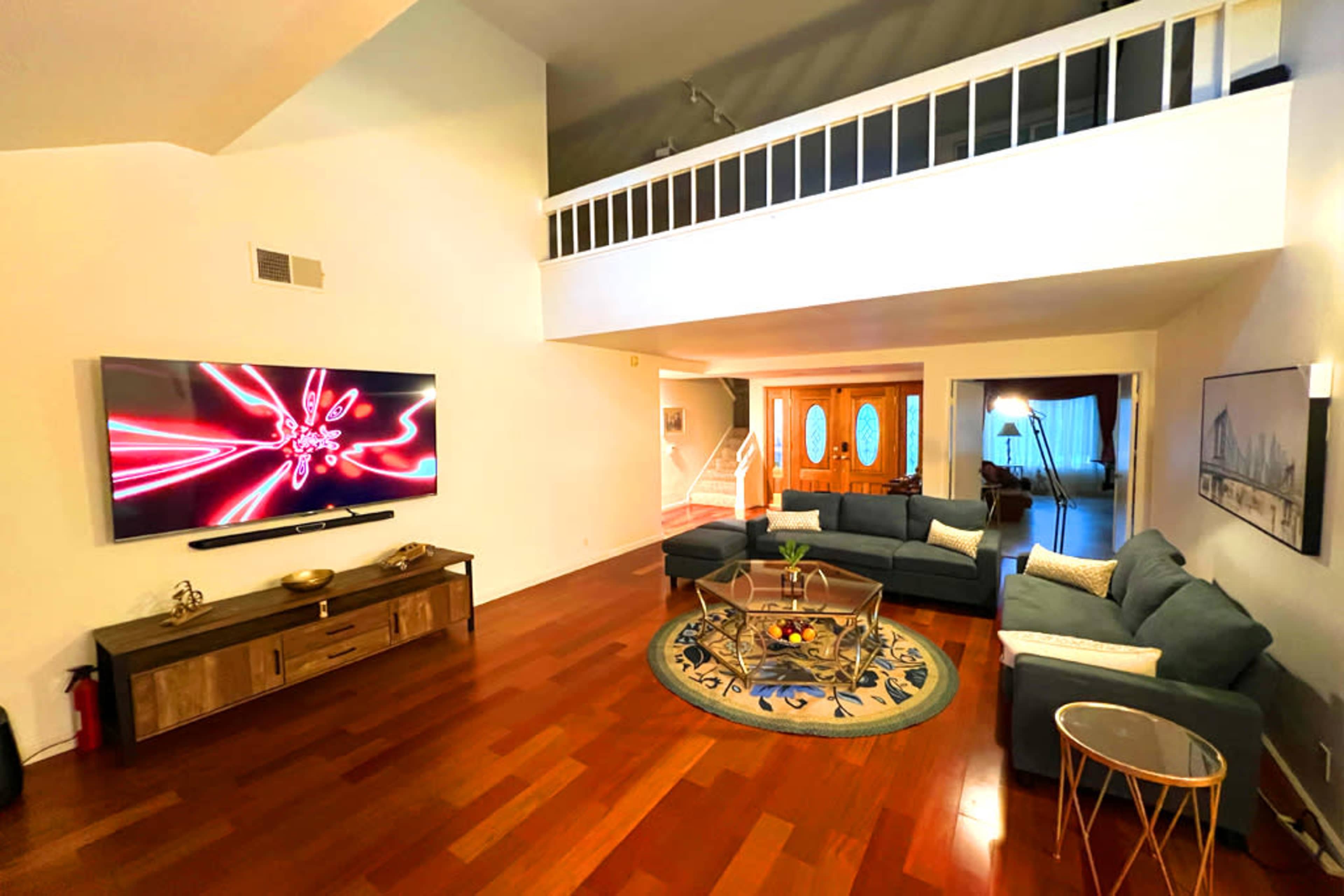 A spacious living room with a large sectional sofa, a decorative rug, a television mounted on the wall, and a few decorative elements, including a coffee table and side table.