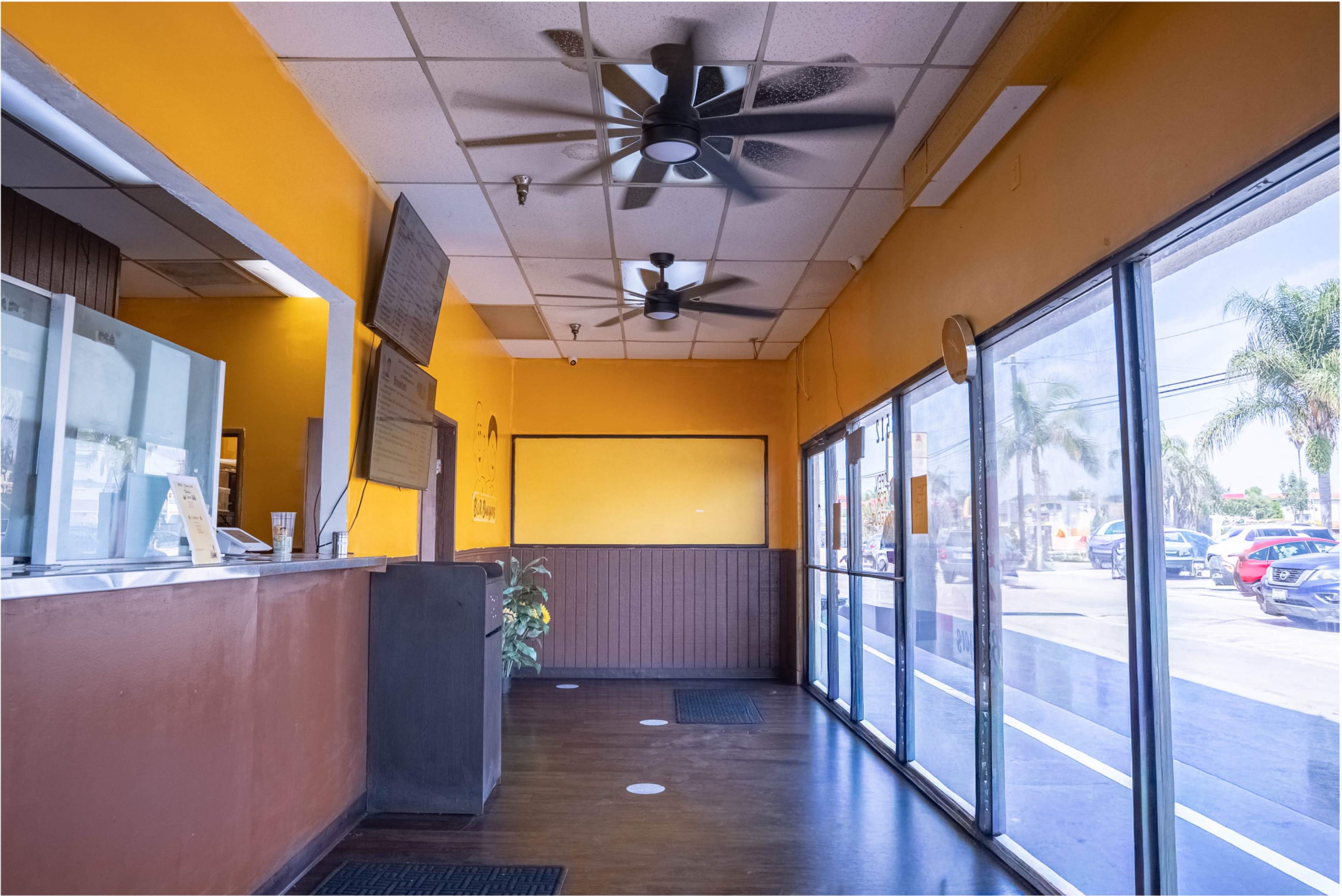 The image shows the interior of a restaurant with a reception area, a counter, and large glass windows letting in natural light.
