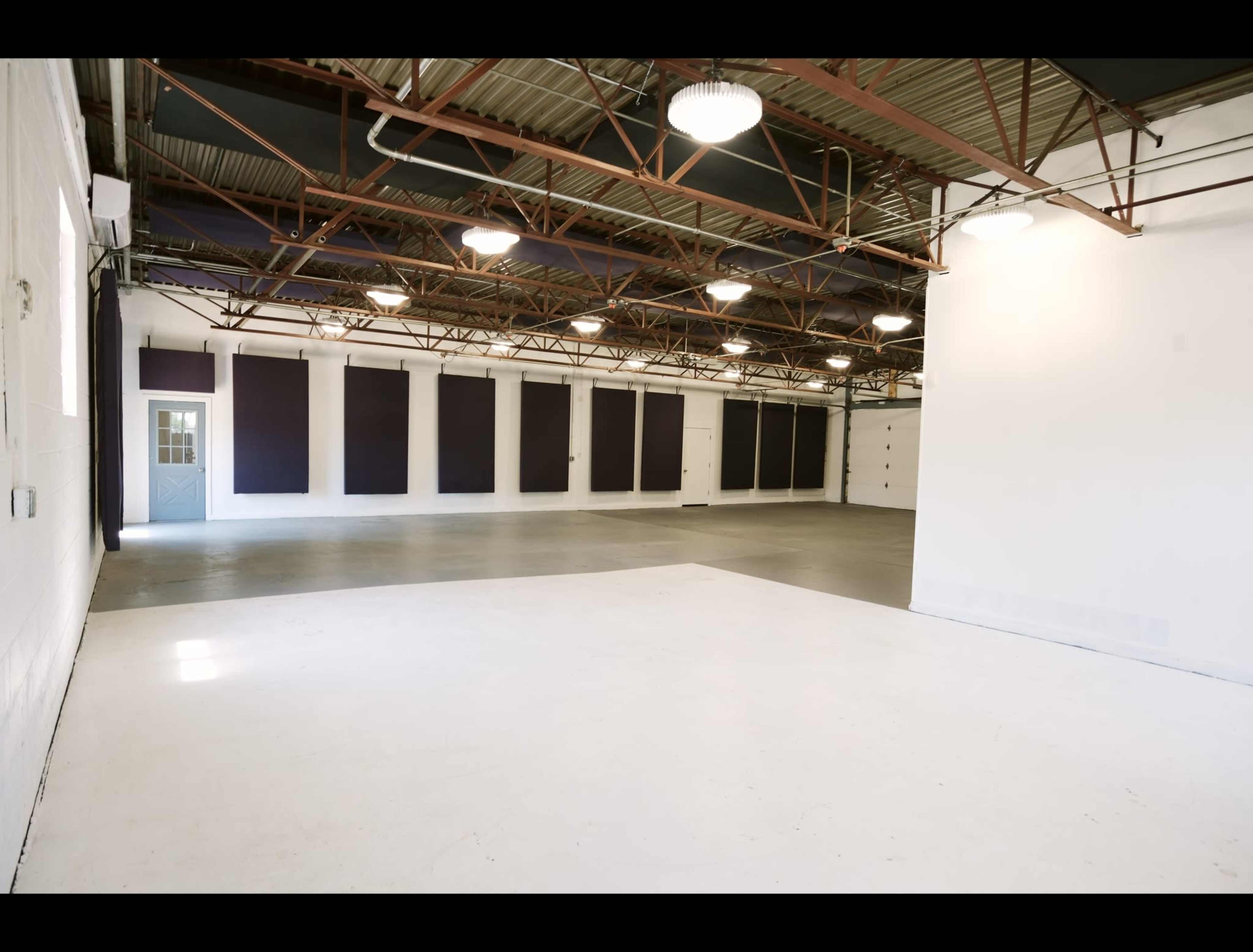 The image shows a spacious industrial-style room with high ceilings, concrete floors, and organized wall panels.