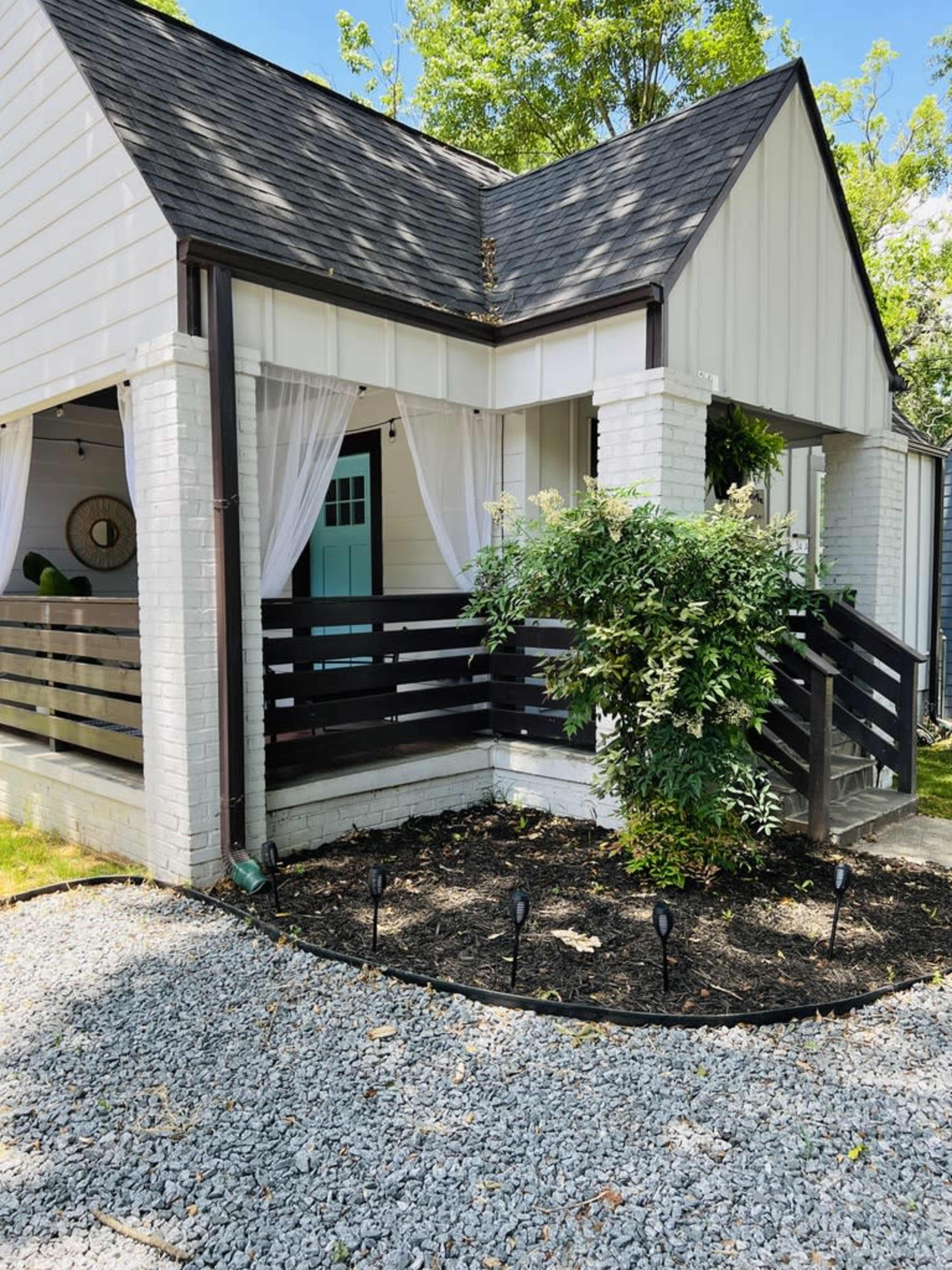 A single-story house features a light-colored exterior, a porch with black railings, and a garden area with gravel landscaping.