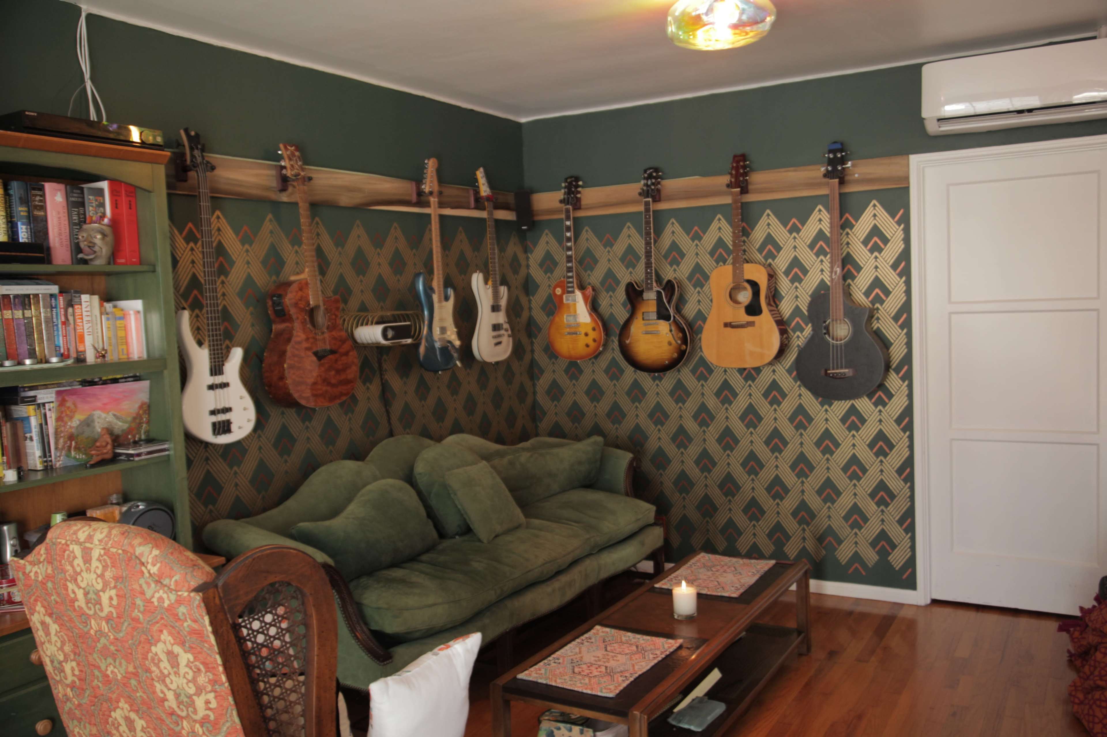 A cozy living room features a green sofa, two coffee tables, and several guitars displayed on a patterned wall.