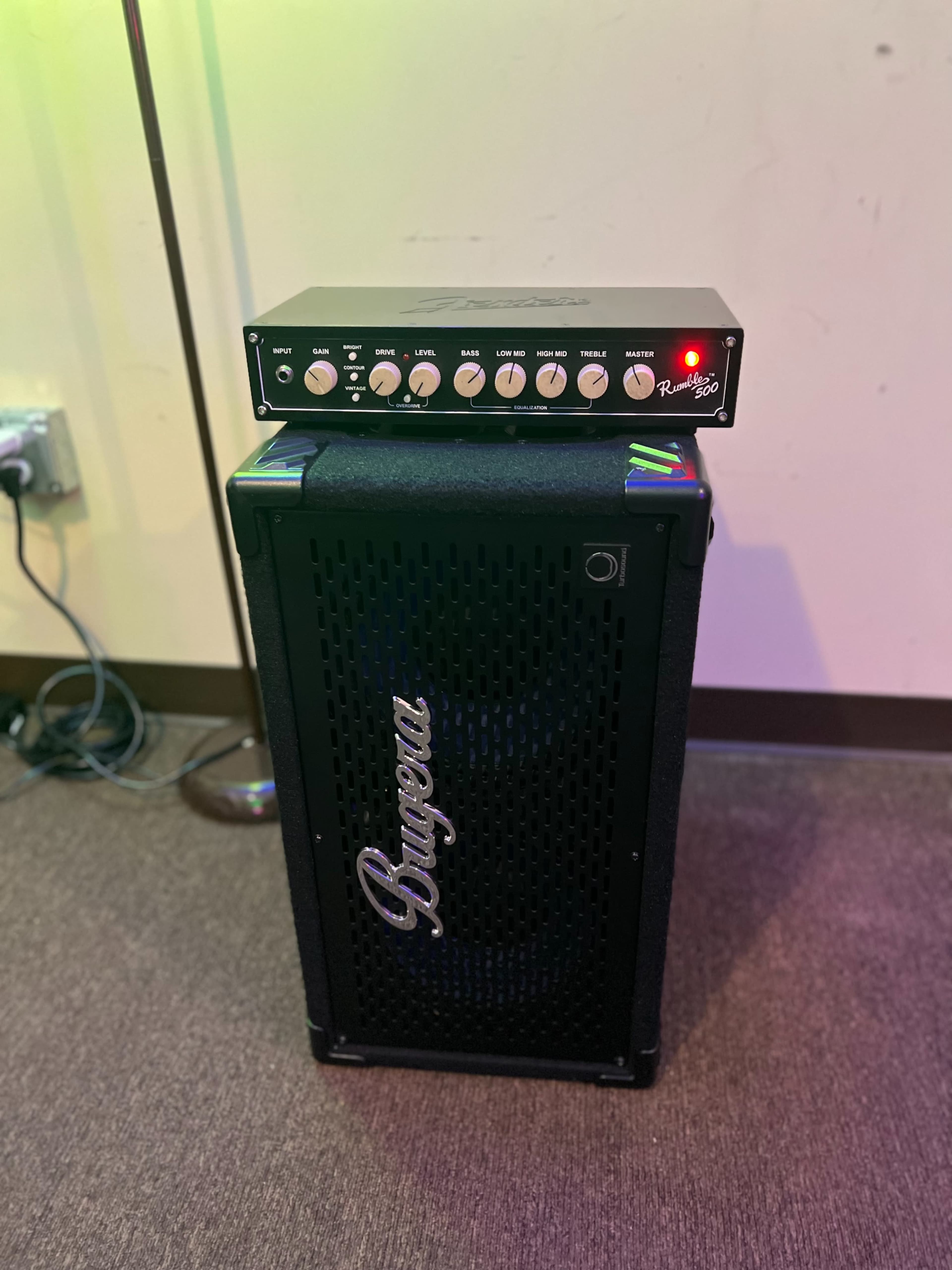 A black speaker cabinet with a control panel on top is positioned against a wall, featuring various knobs and a red indicator light.