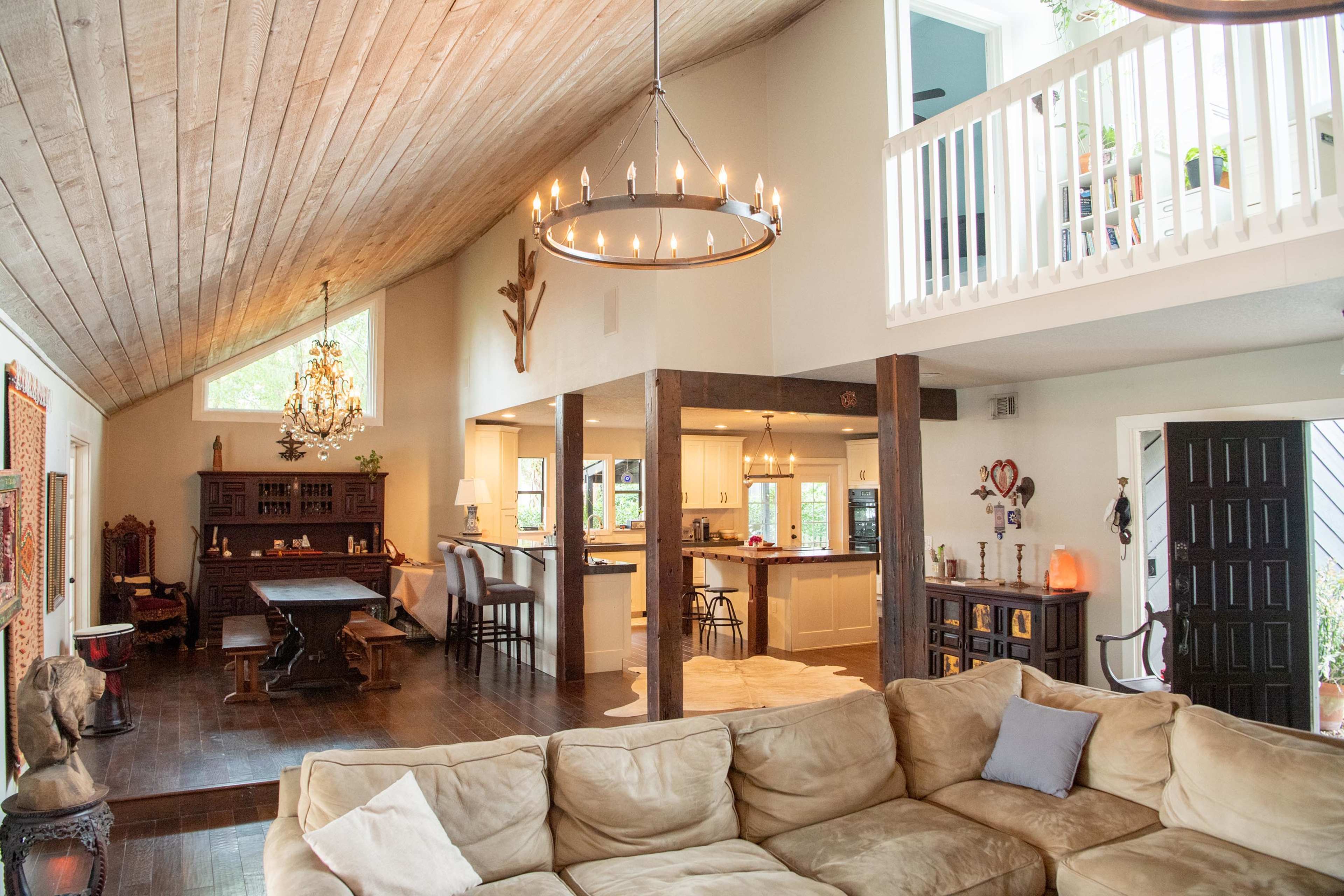 A spacious, open-concept living room and kitchen area with a high wooden ceiling and several light fixtures.