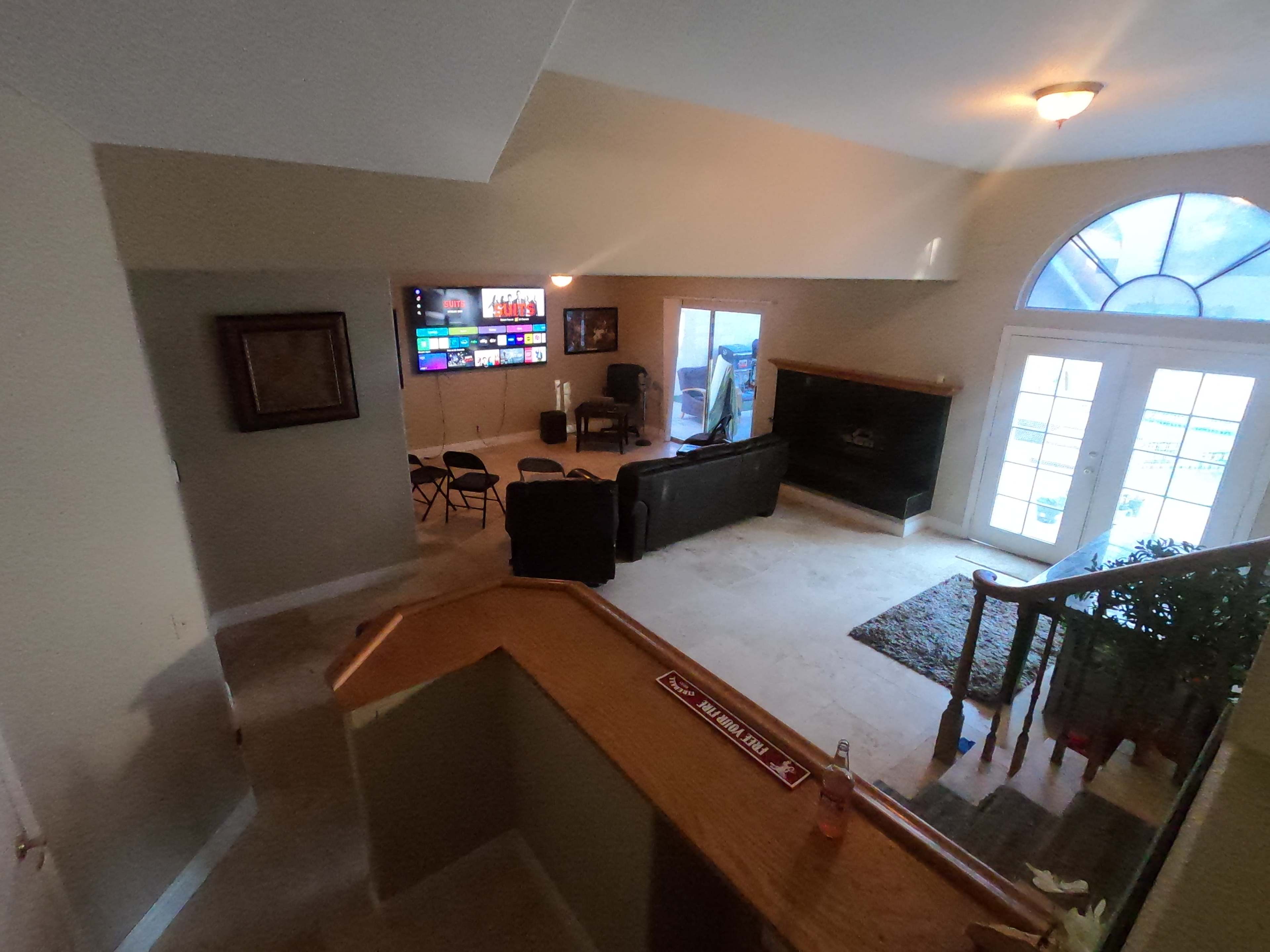 The image shows a spacious living room with a large window, a TV on the wall, two couches, and a staircase leading down to the main area.