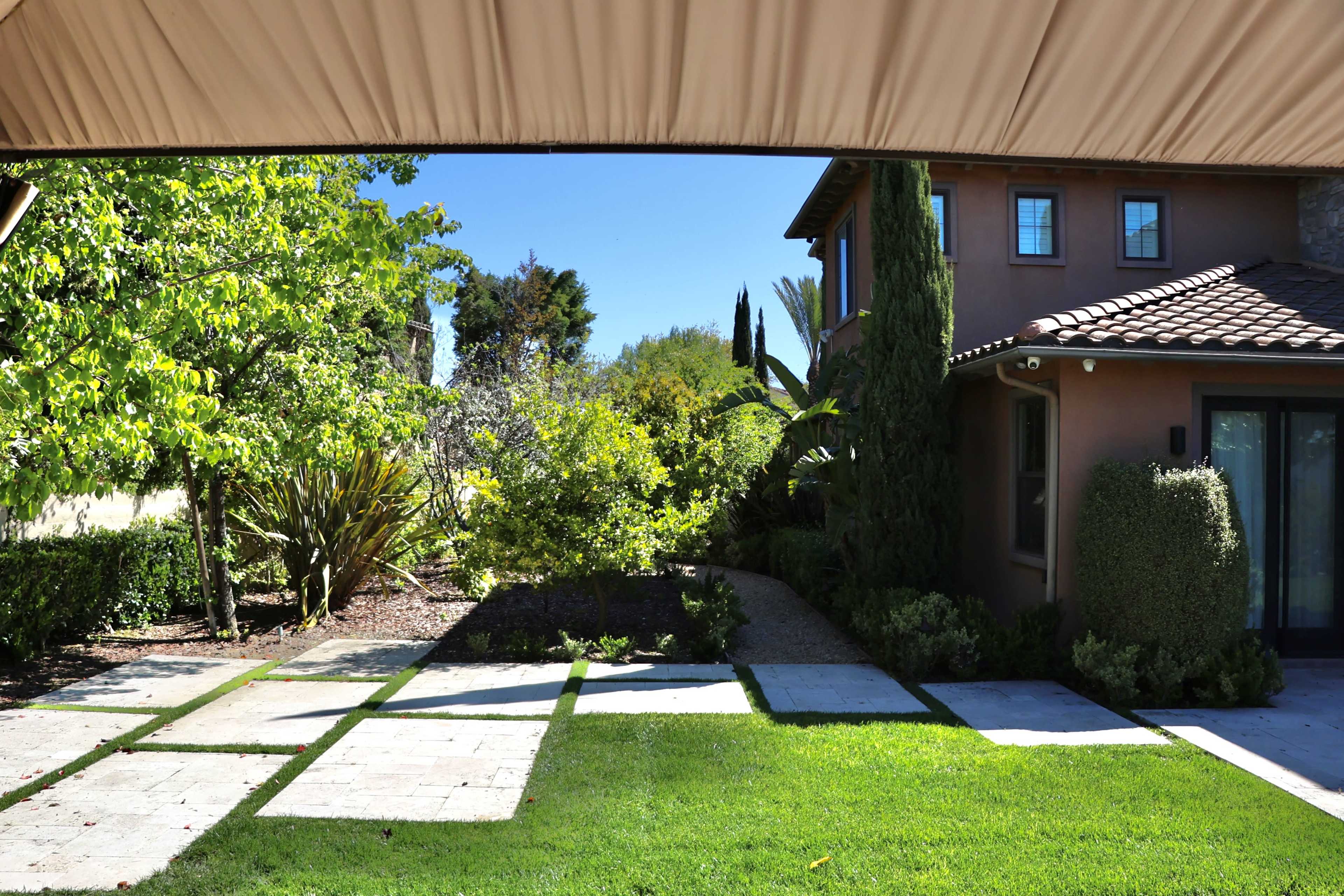 A pathway of square stone slabs leads through a neatly landscaped garden to a house featuring a brown exterior and a tiled roof.