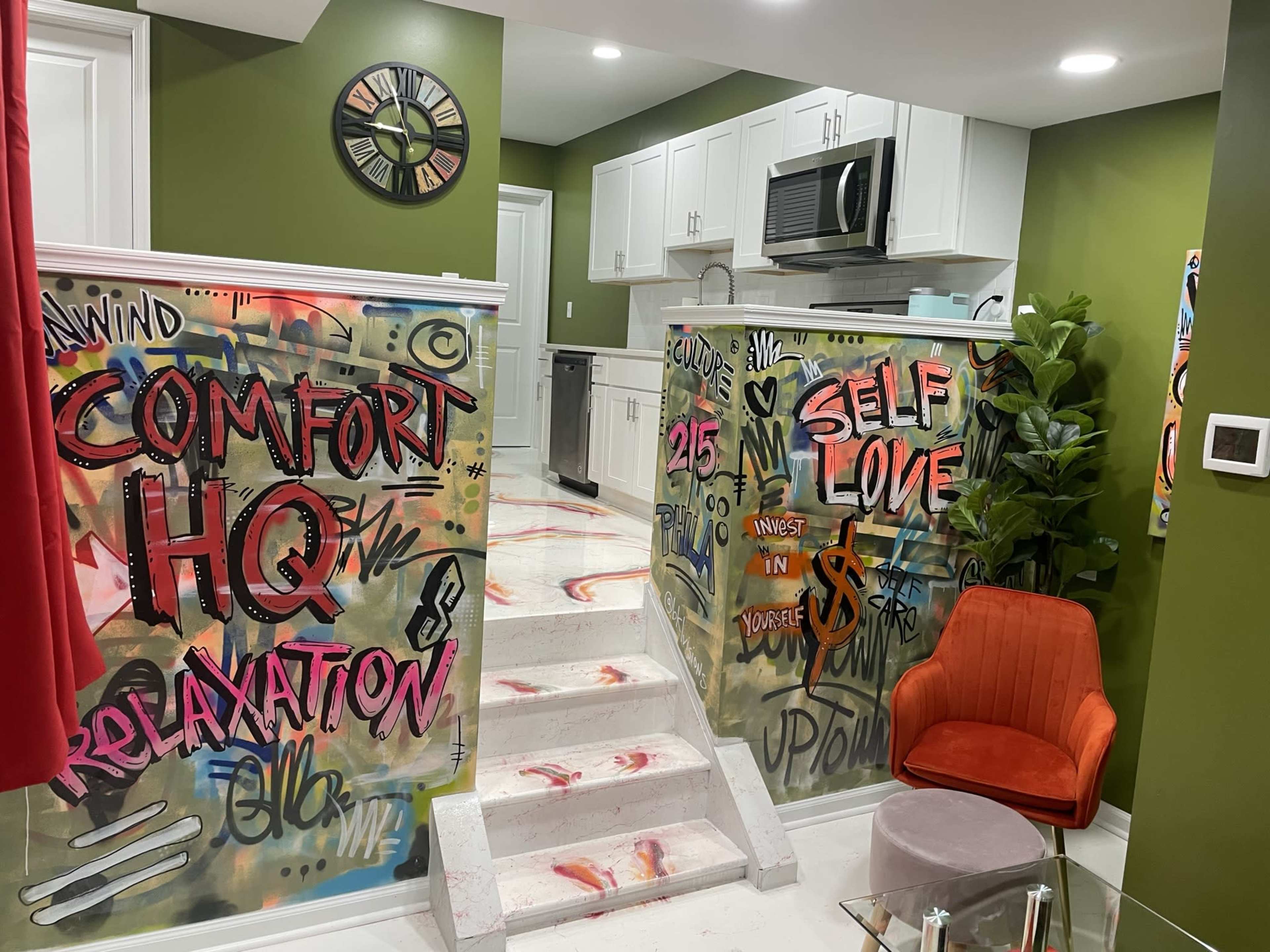 A modern interior space with graffiti-style wall art on transparent partitions, an orange chair, and a kitchen area in the background.