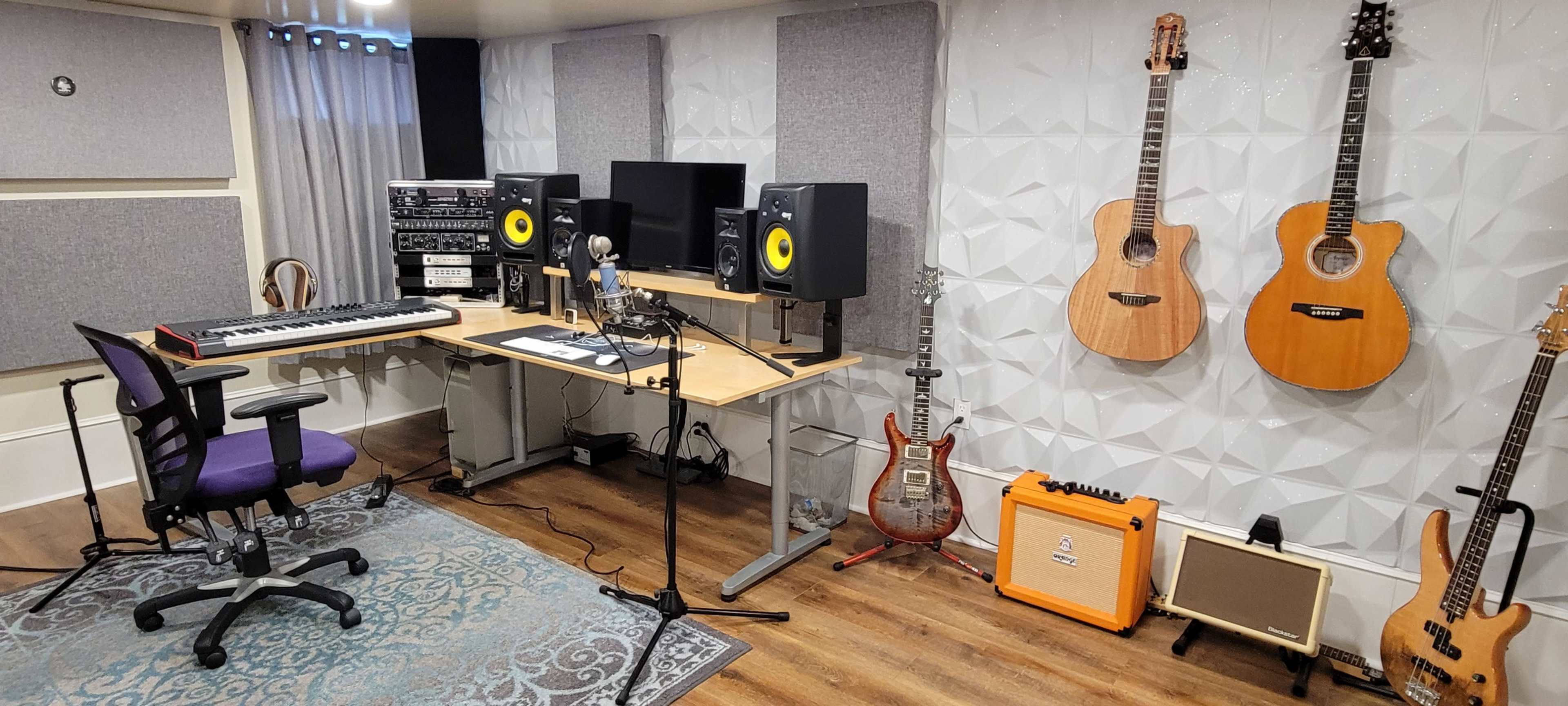 A music recording studio with various instruments, including acoustic guitars, a keyboard, studio monitors, and audio equipment, arranged around a desk with a microphone and chair.