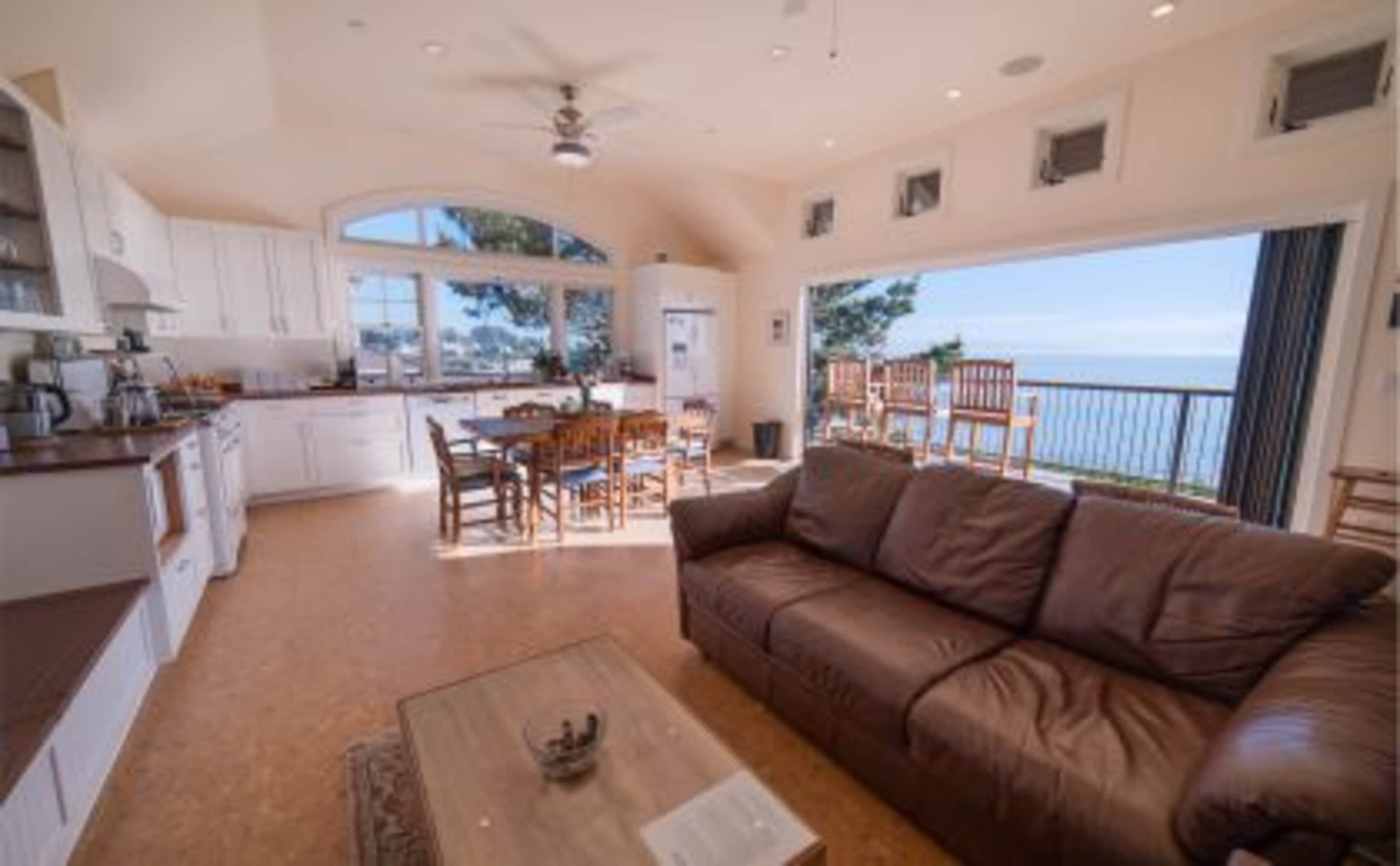 A modern, airy living space with a kitchen and dining area that overlooks a balcony and scenic water view.