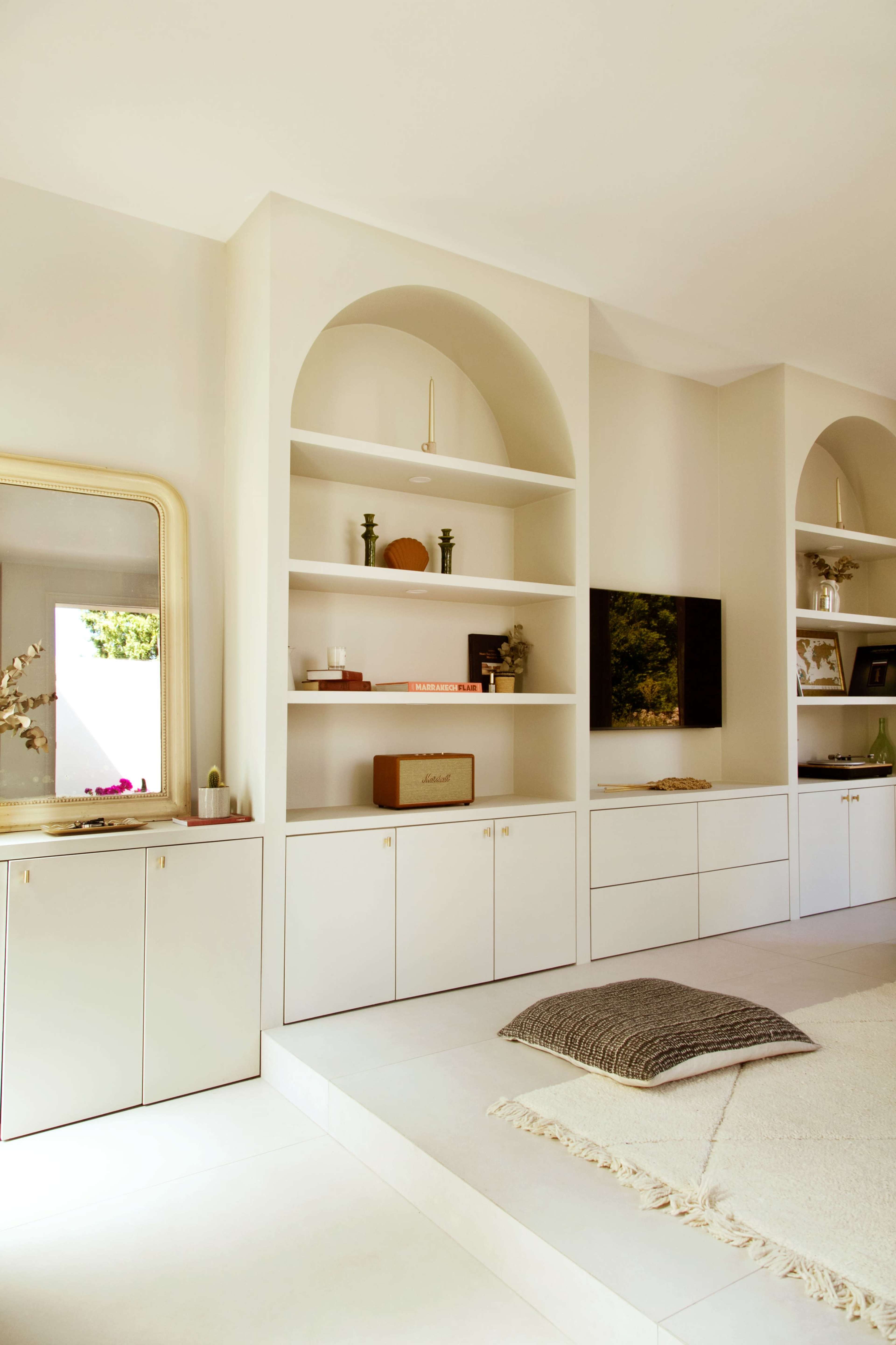 The image features a modern interior with built-in shelves, a television, and a minimalist seating area on a light-colored floor.