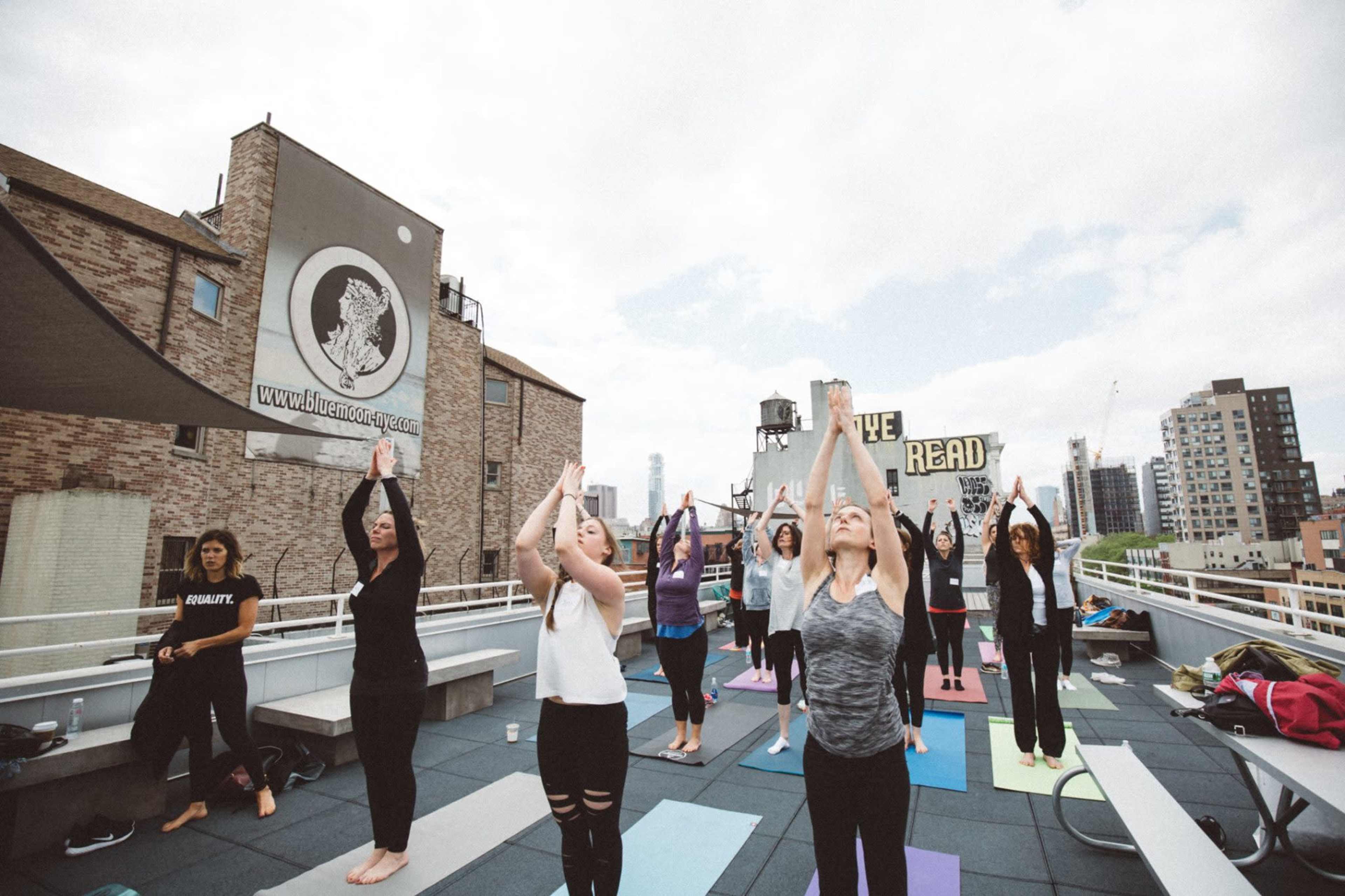 A group of people practices yoga on a rooftop surrounded by urban buildings.