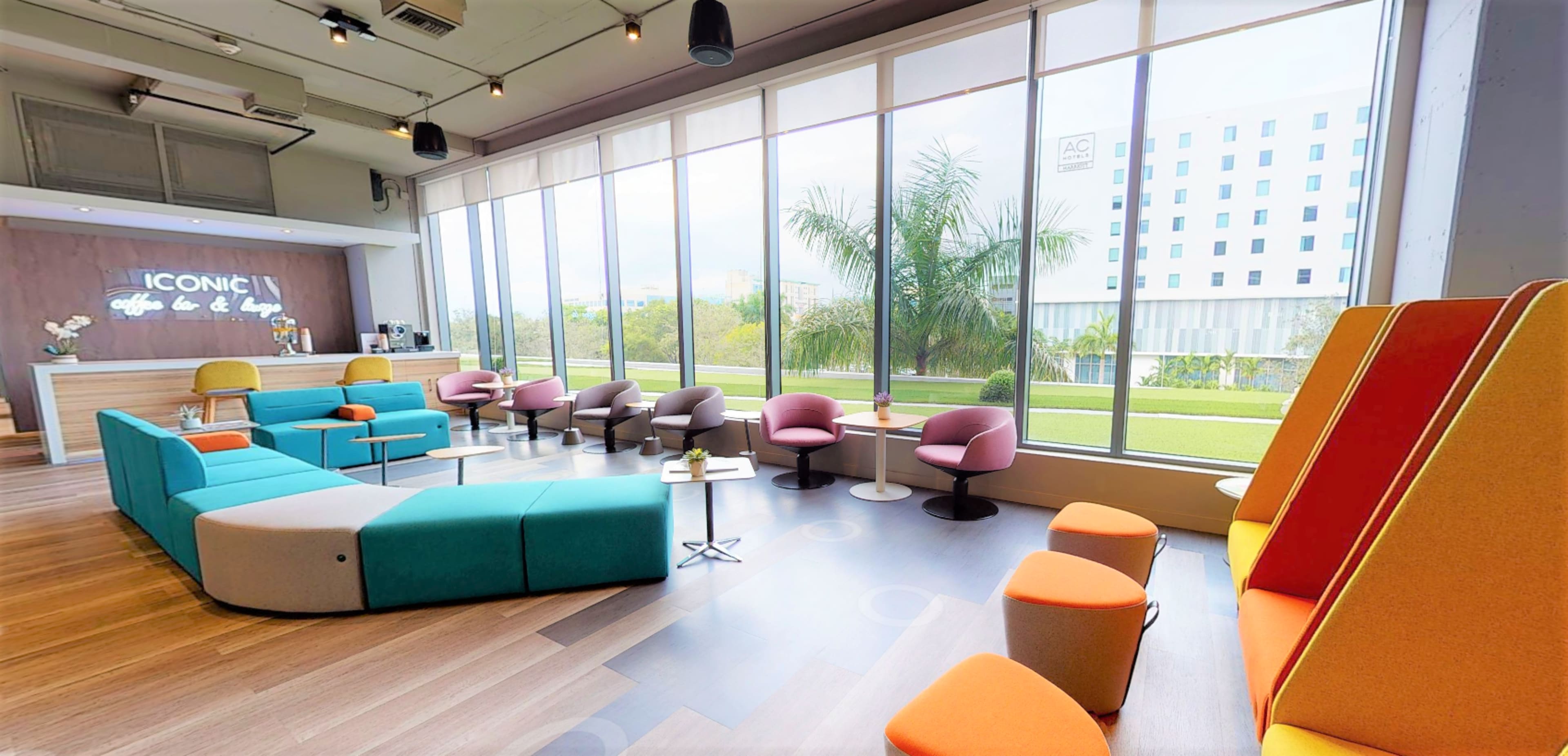 A modern lounge area with colorful seating arrangements, large windows allowing natural light, and a view of greenery outside.