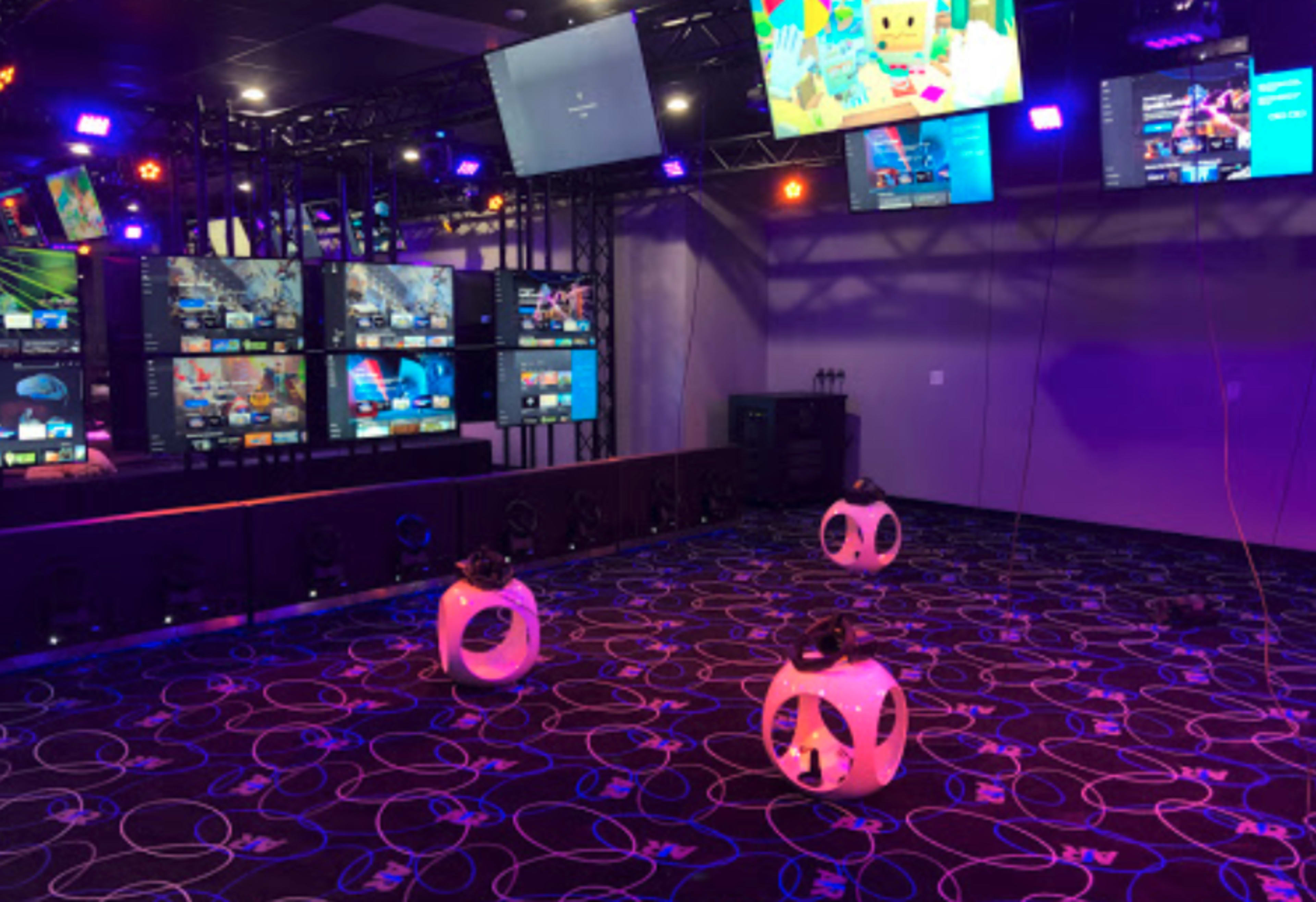 A gaming room equipped with multiple screens and three virtual reality headsets placed on the floor.