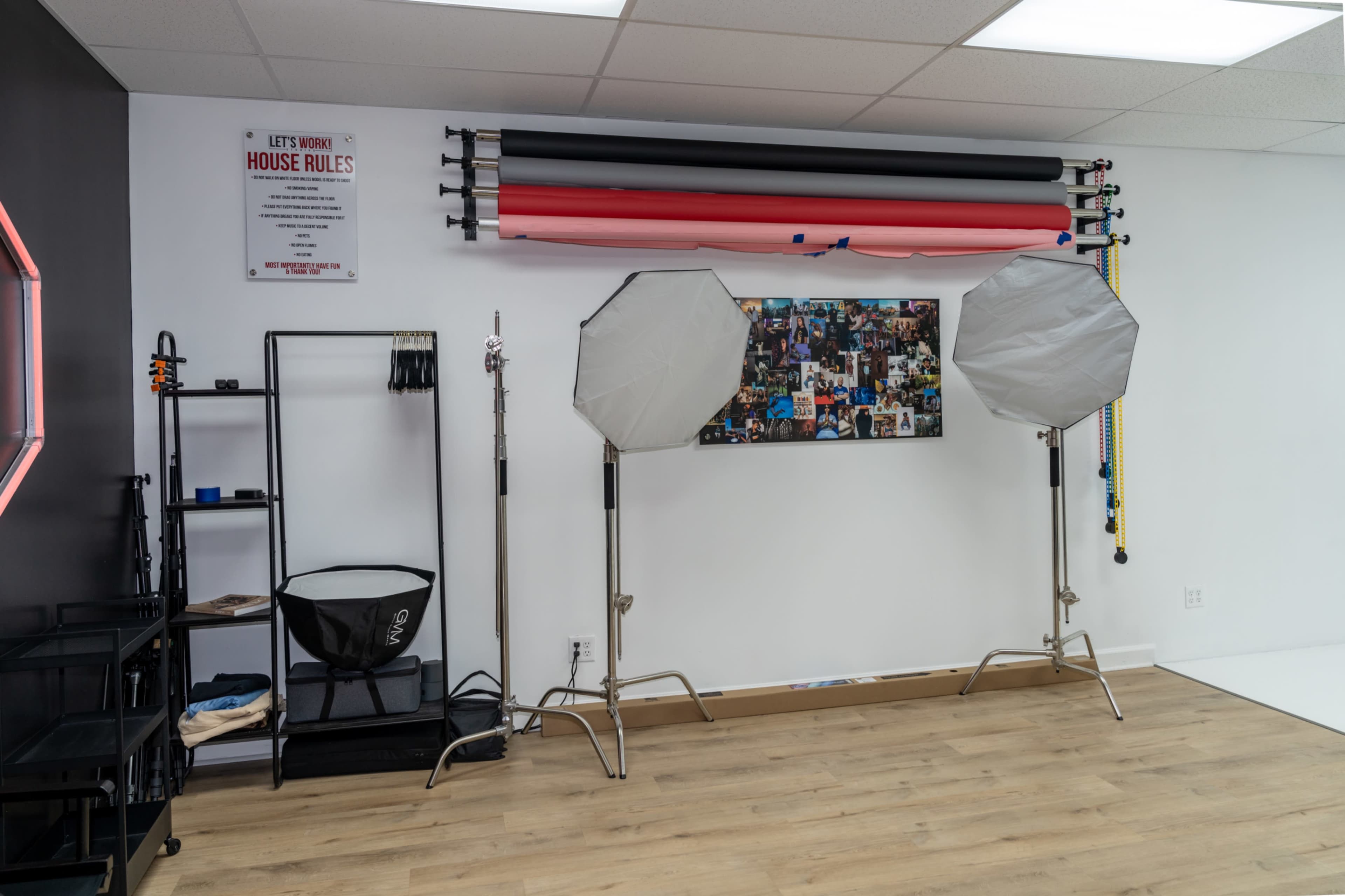 The image shows a photography studio with backdrop rolls, lighting equipment, and a display of photographs on the wall.