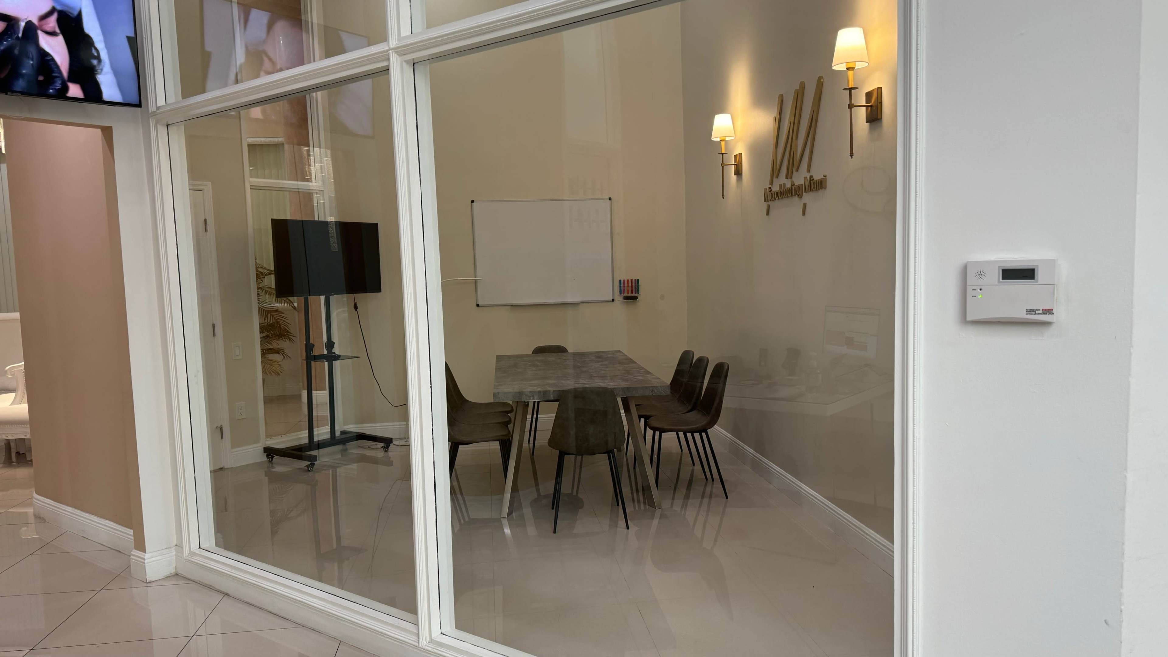 A meeting room with a large table and chairs is visible through a glass wall, featuring a whiteboard and a television display.
