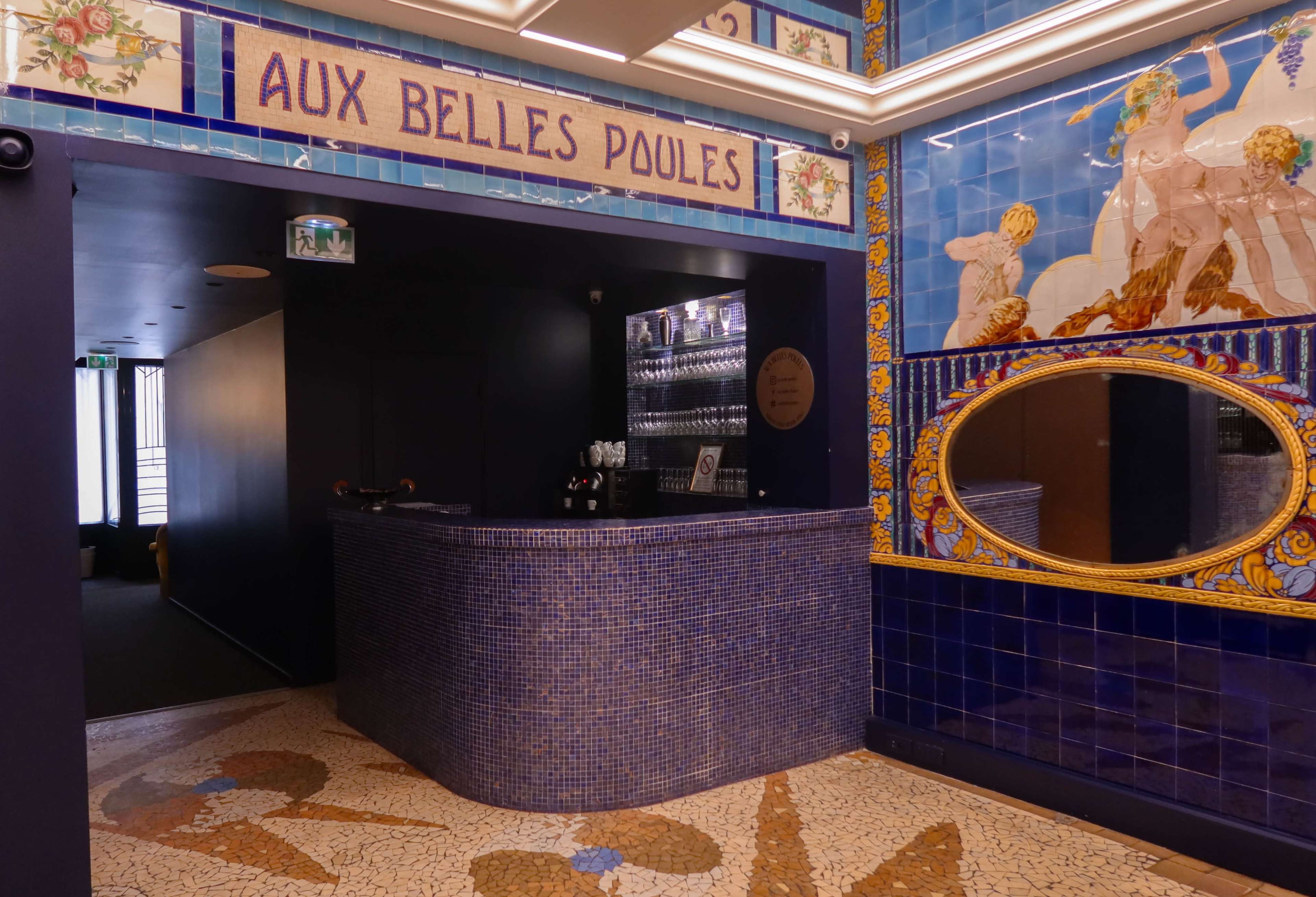 A tiled bar area with a mosaic floor and decorative wall tiles featuring a mirror and illustrations.