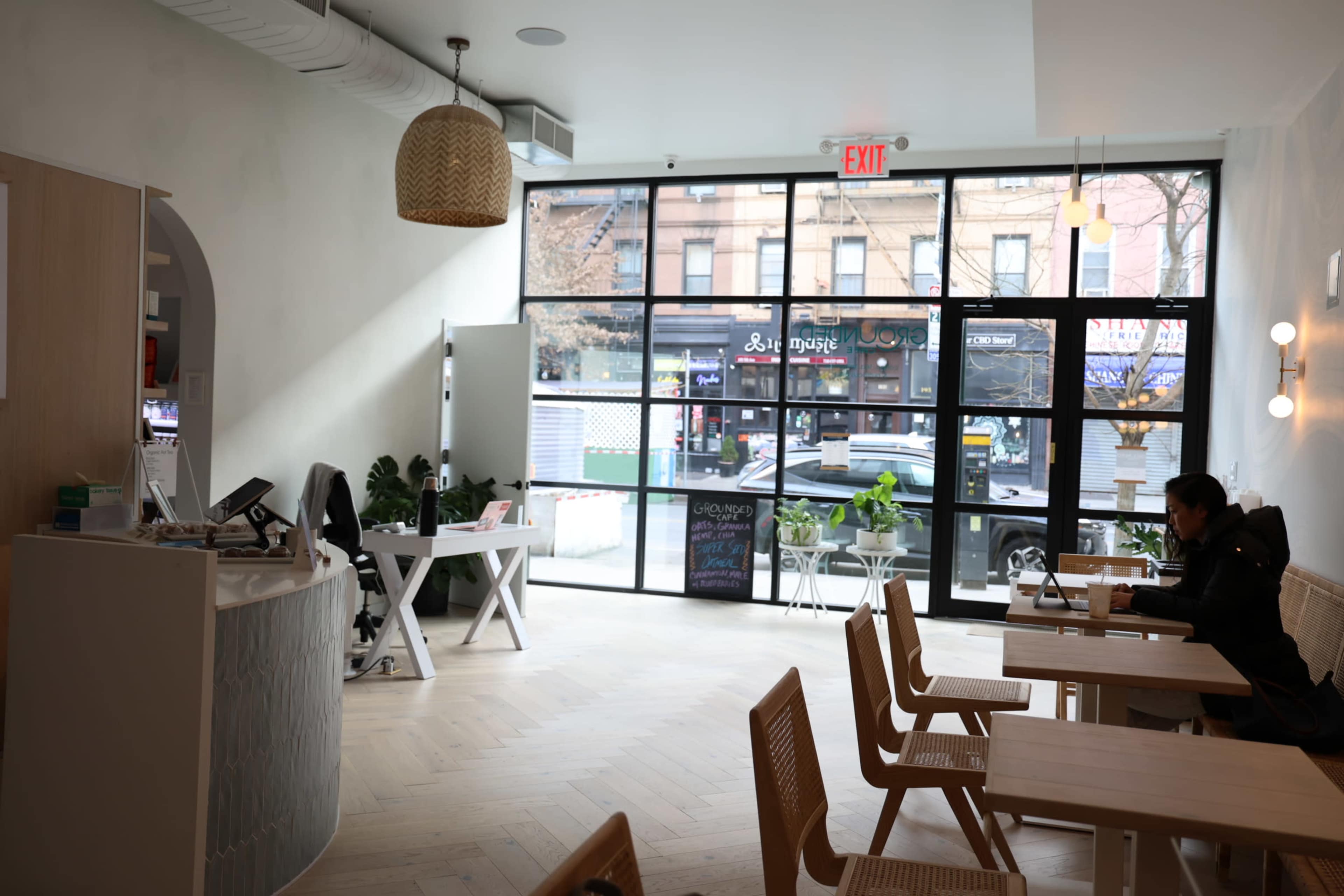 A bright, minimalist café features wooden tables, a service counter, and large windows showcasing a city street.