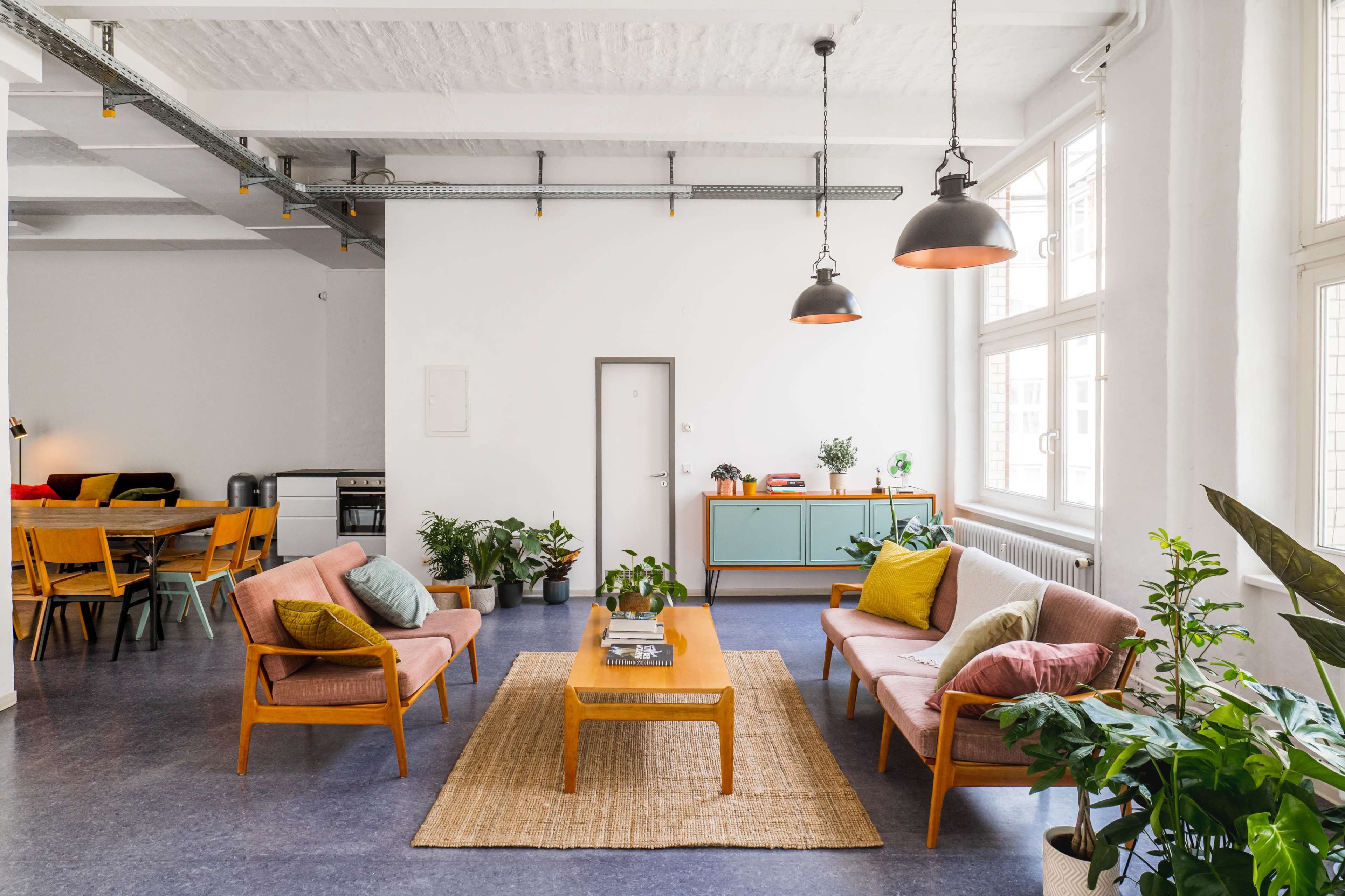 A bright living area with two chairs, a coffee table, and multiple plants, alongside a dining area featuring a wooden table and chairs.