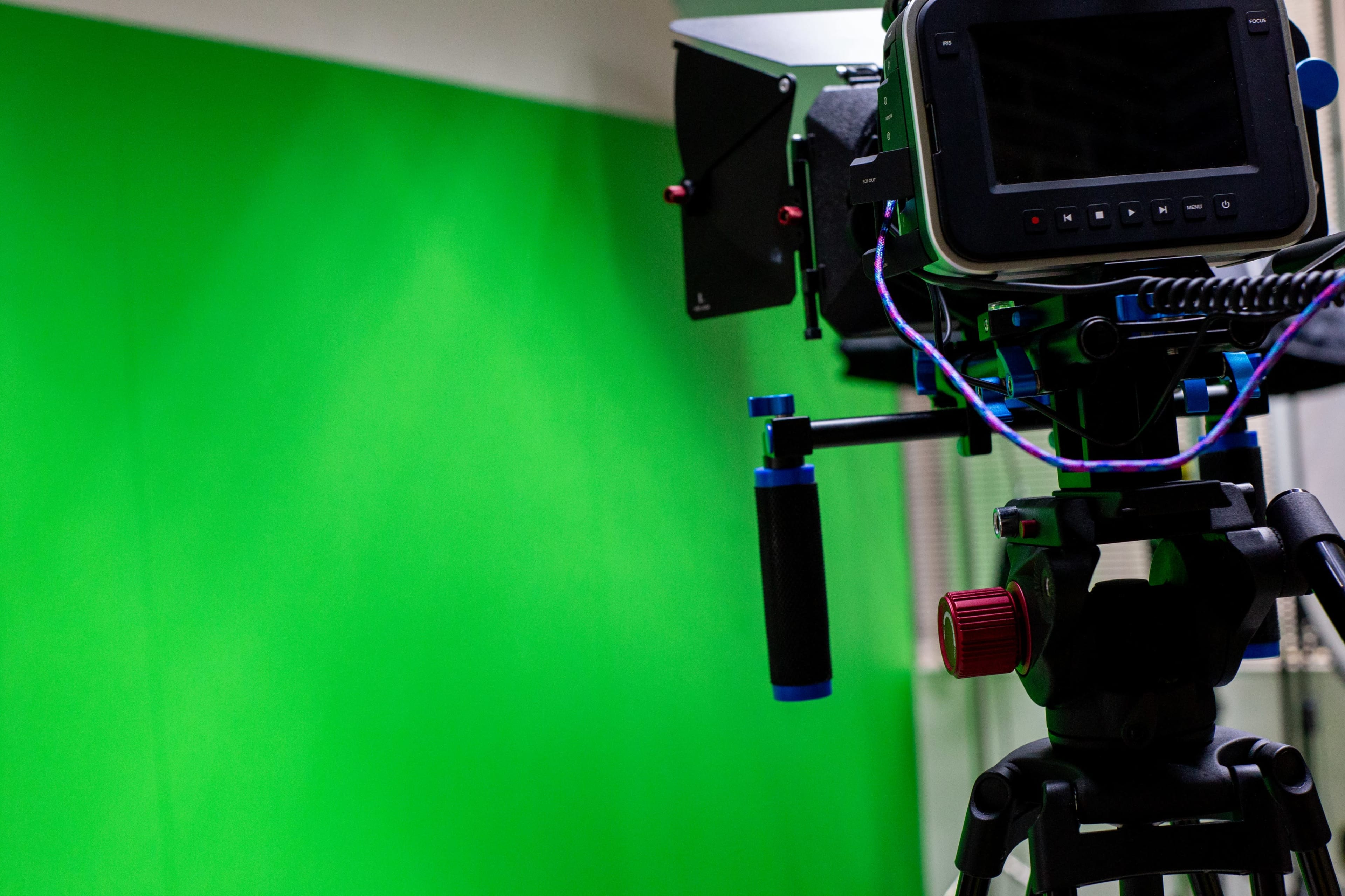 A video camera is positioned on a tripod in front of a green screen.