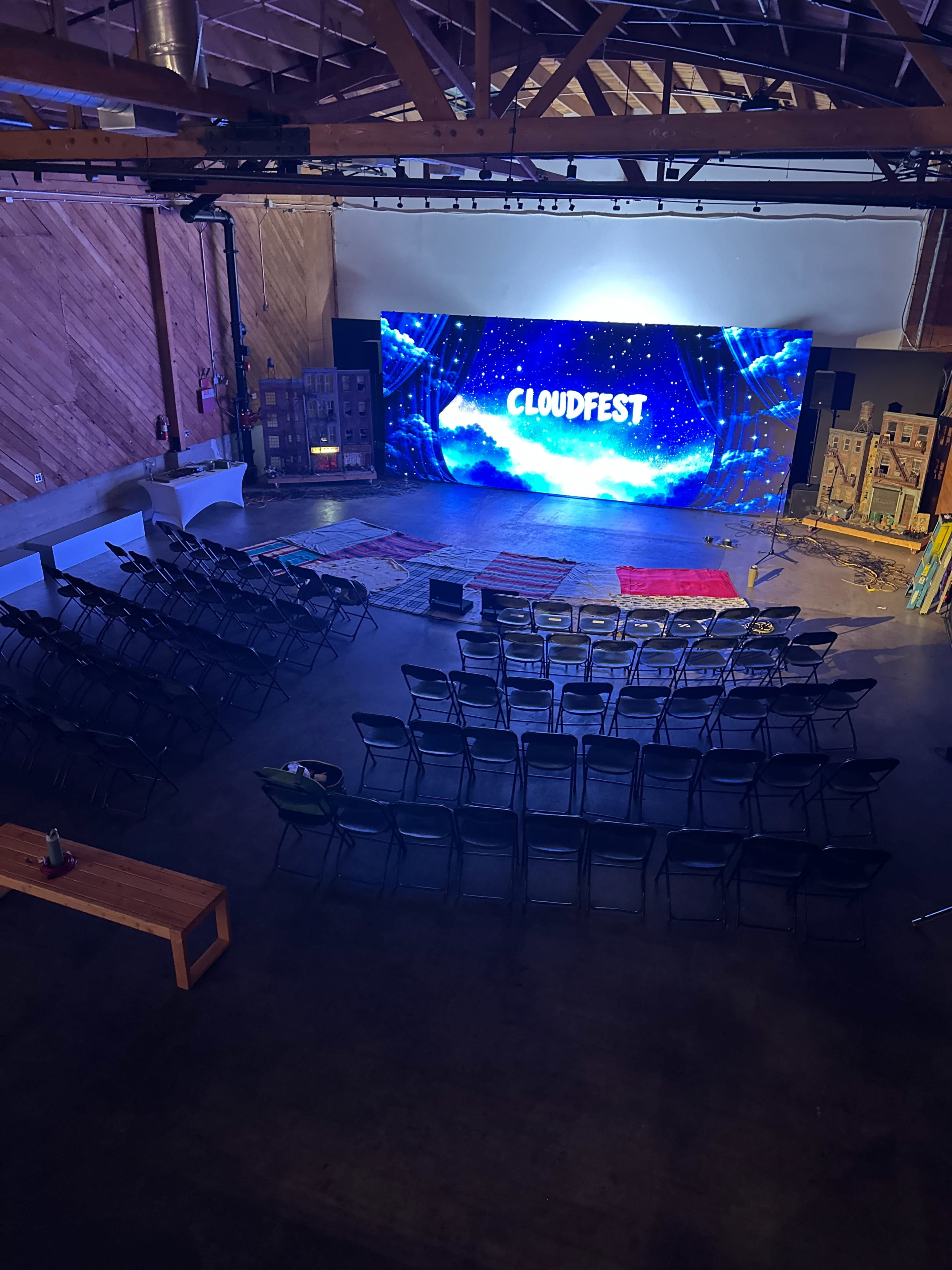 The image shows an indoor event space with rows of chairs arranged in front of a large screen that displays "CLOUDFEST."