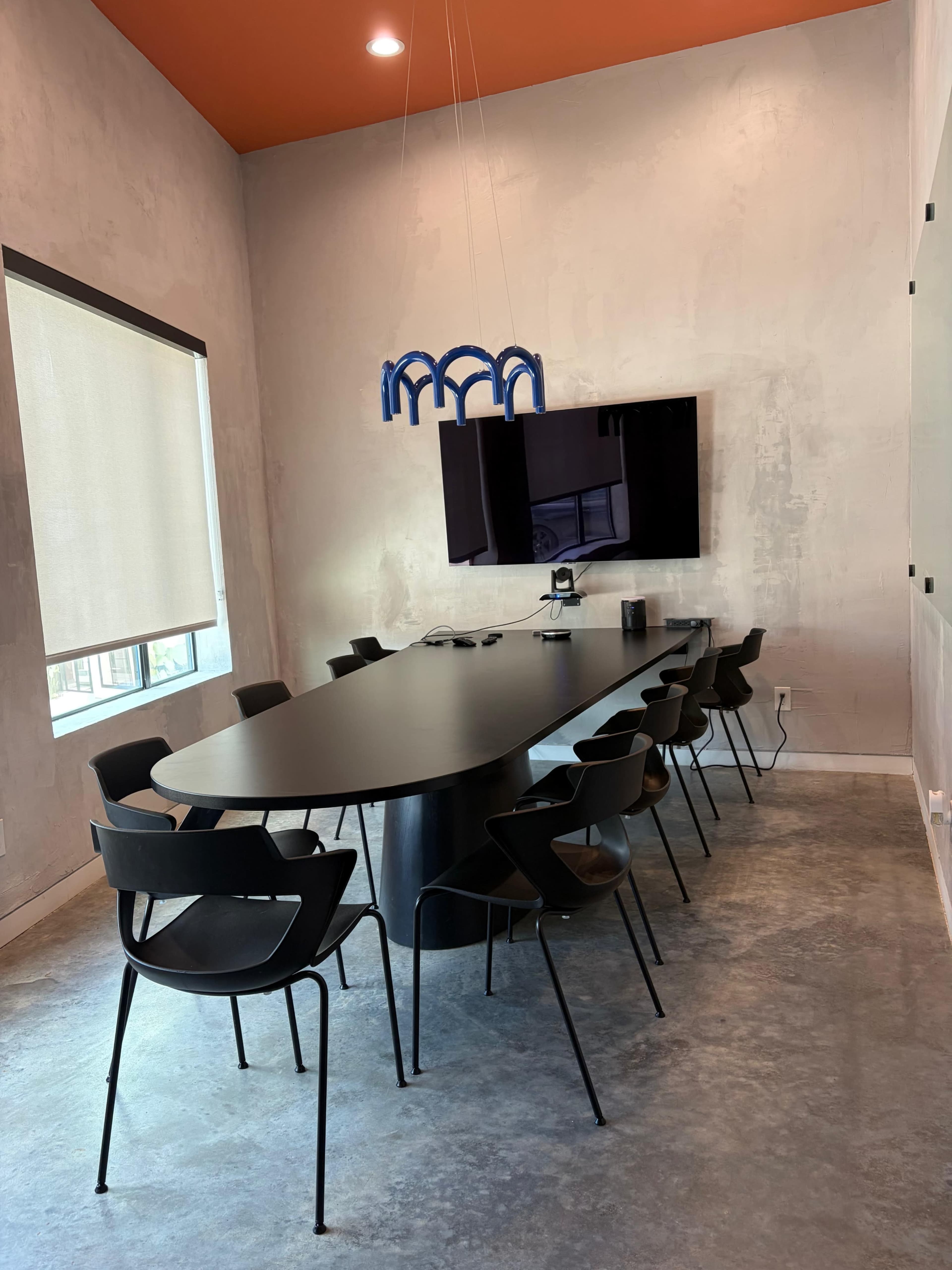 The image shows a modern conference room with a long black table surrounded by black chairs and a wall-mounted television.