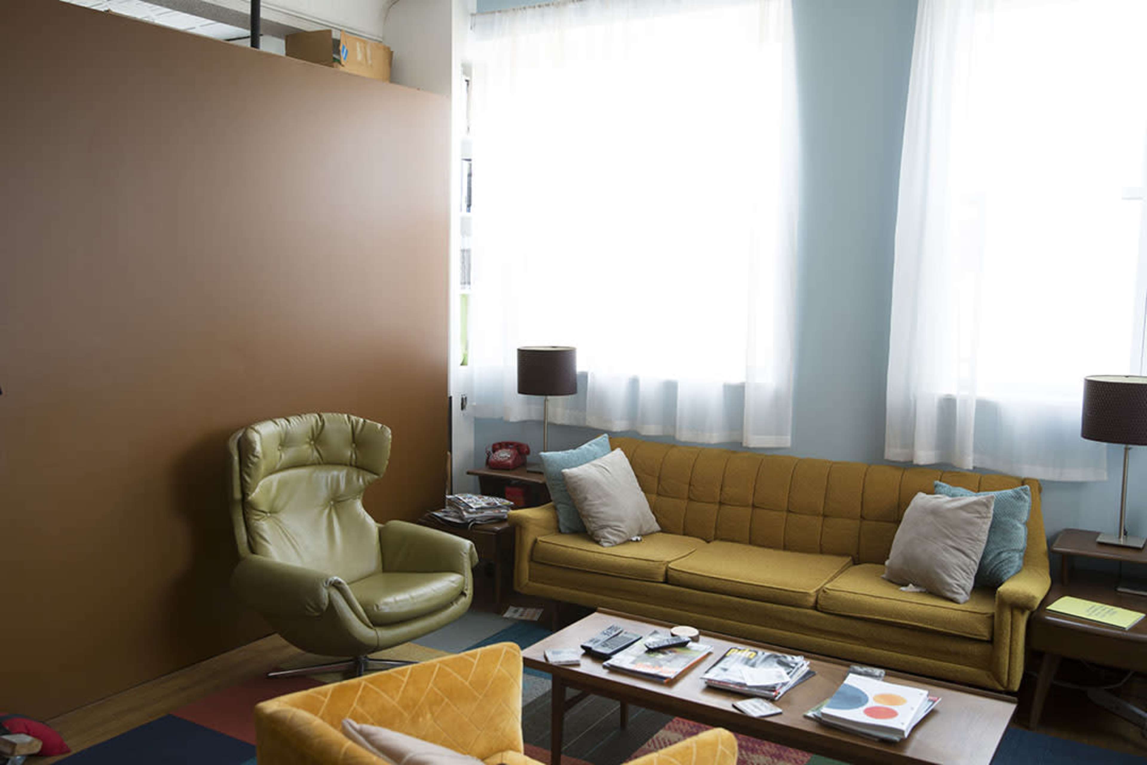 A cozy living room with a yellow couch, a green swivel chair, and large windows letting in natural light.