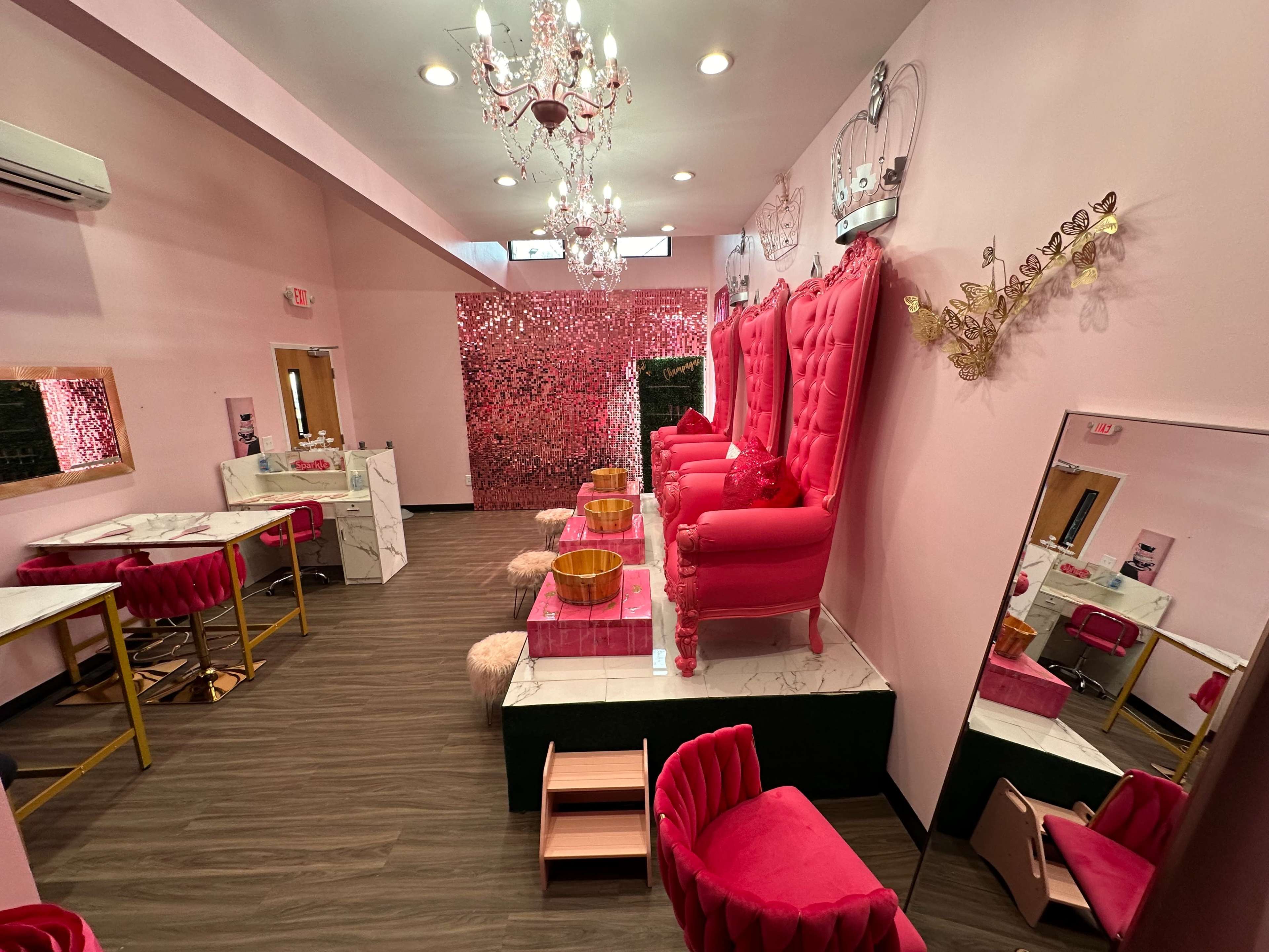 The image shows a beauty salon interior with pink walls, two large pink chairs, a decorative chandelier, and a mirrored wall.