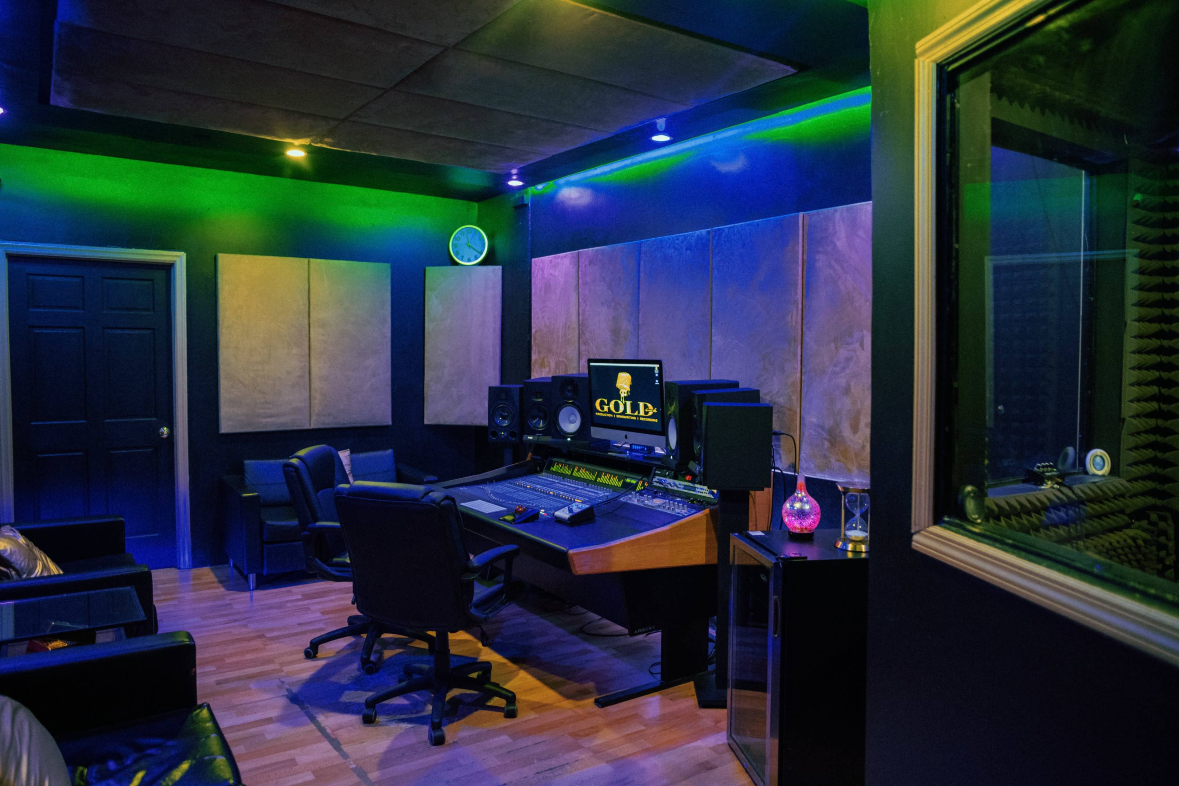 A music studio equipped with a control desk, speakers, and soundproof panels, illuminated by colorful lights.
