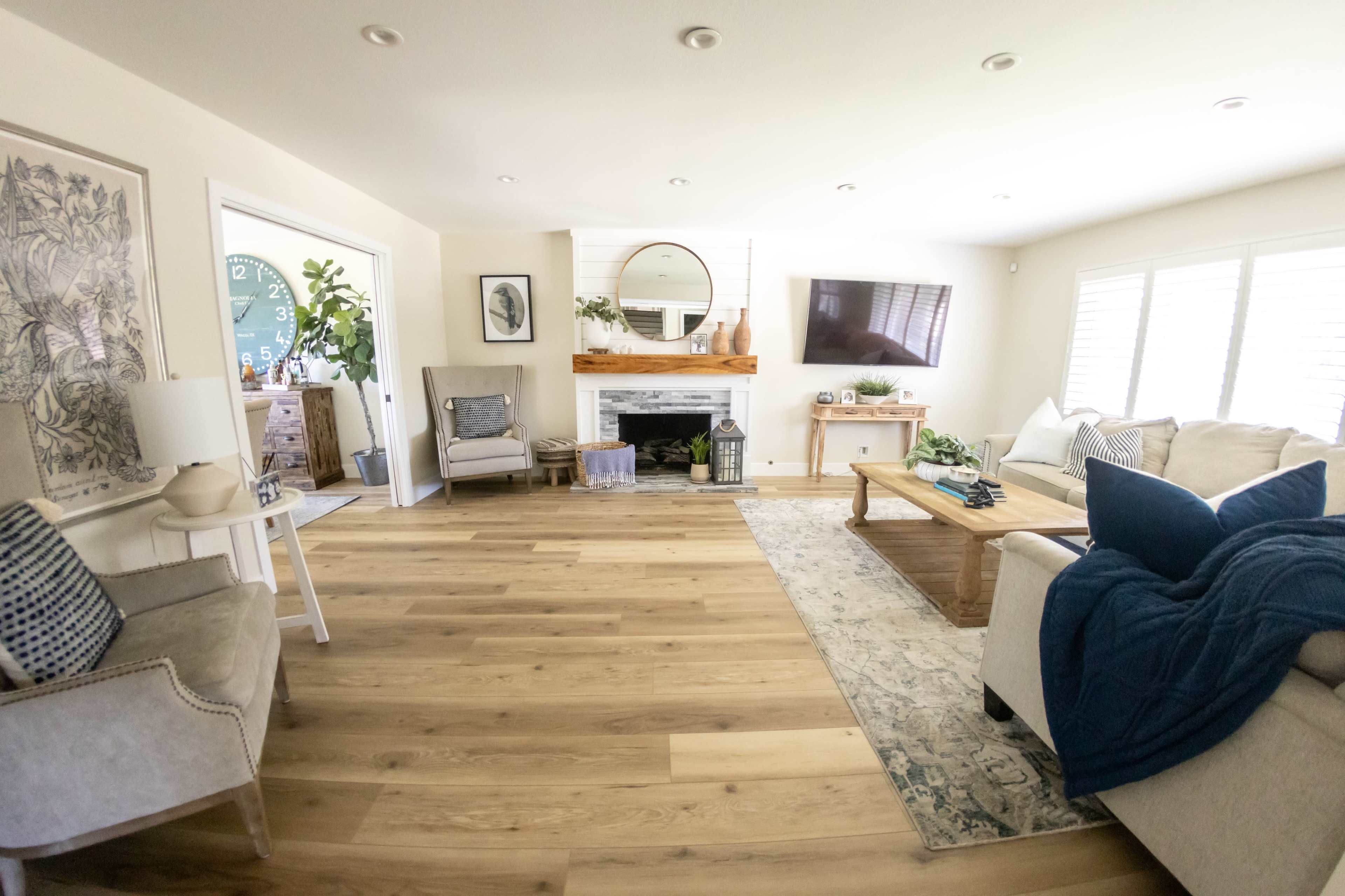 The living room features a light color palette with a fireplace, a large mirror above the mantel, comfortable seating, and hardwood flooring.