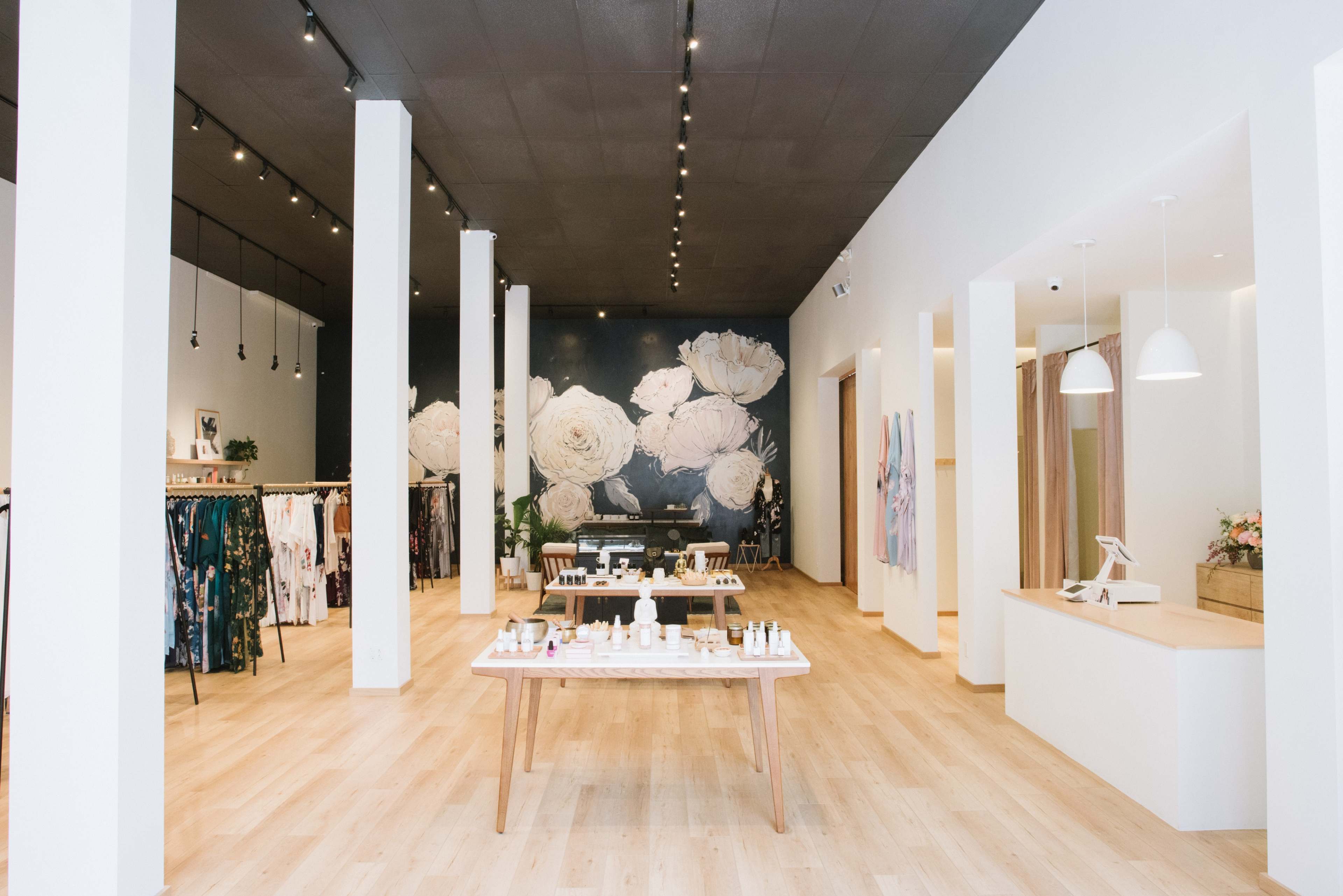 A spacious retail store with a central display table, clothing racks along the sides, and a floral mural on the back wall.