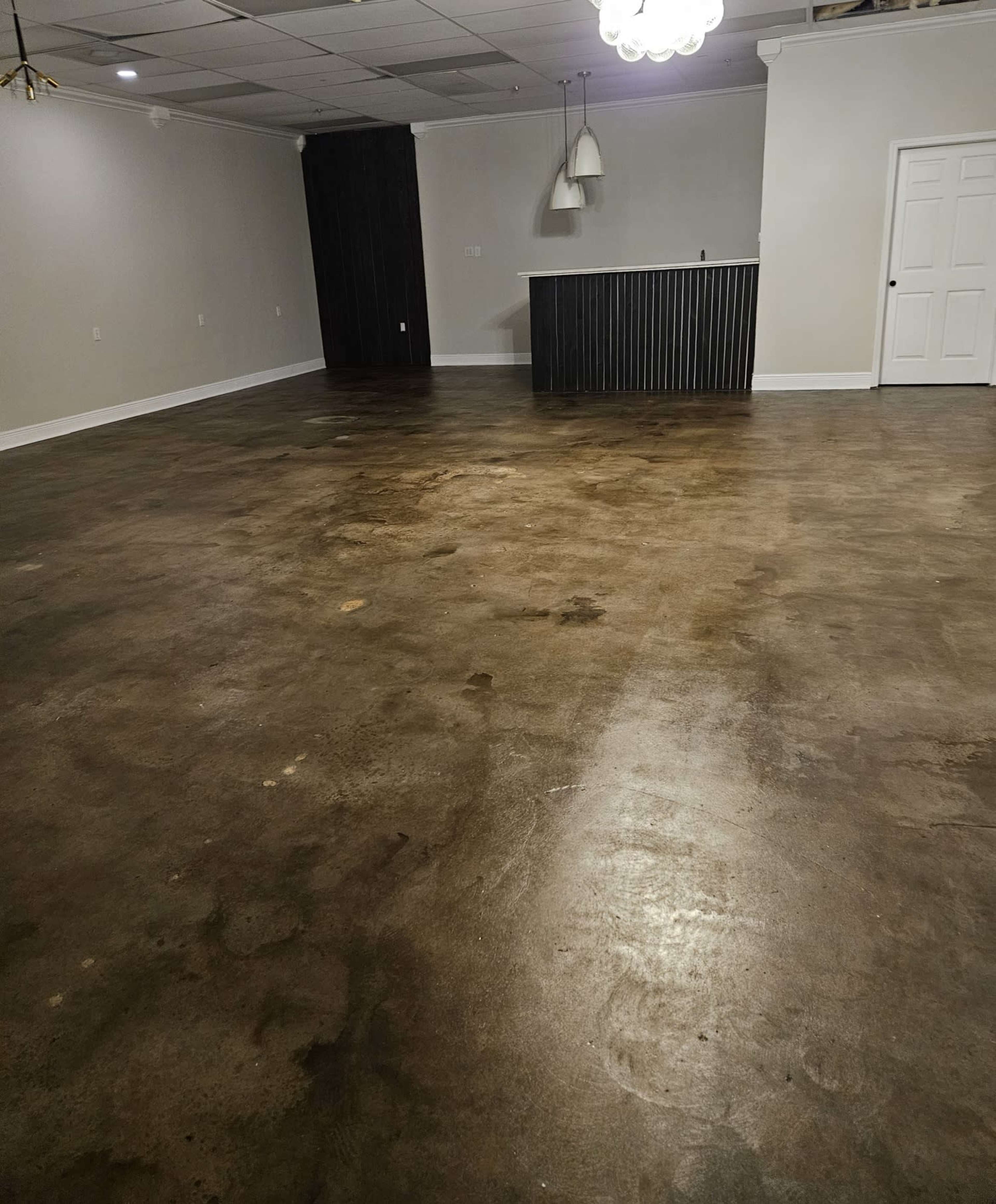 The image shows a spacious room with a polished concrete floor, a bar-style counter in the background, and a door on the right side.