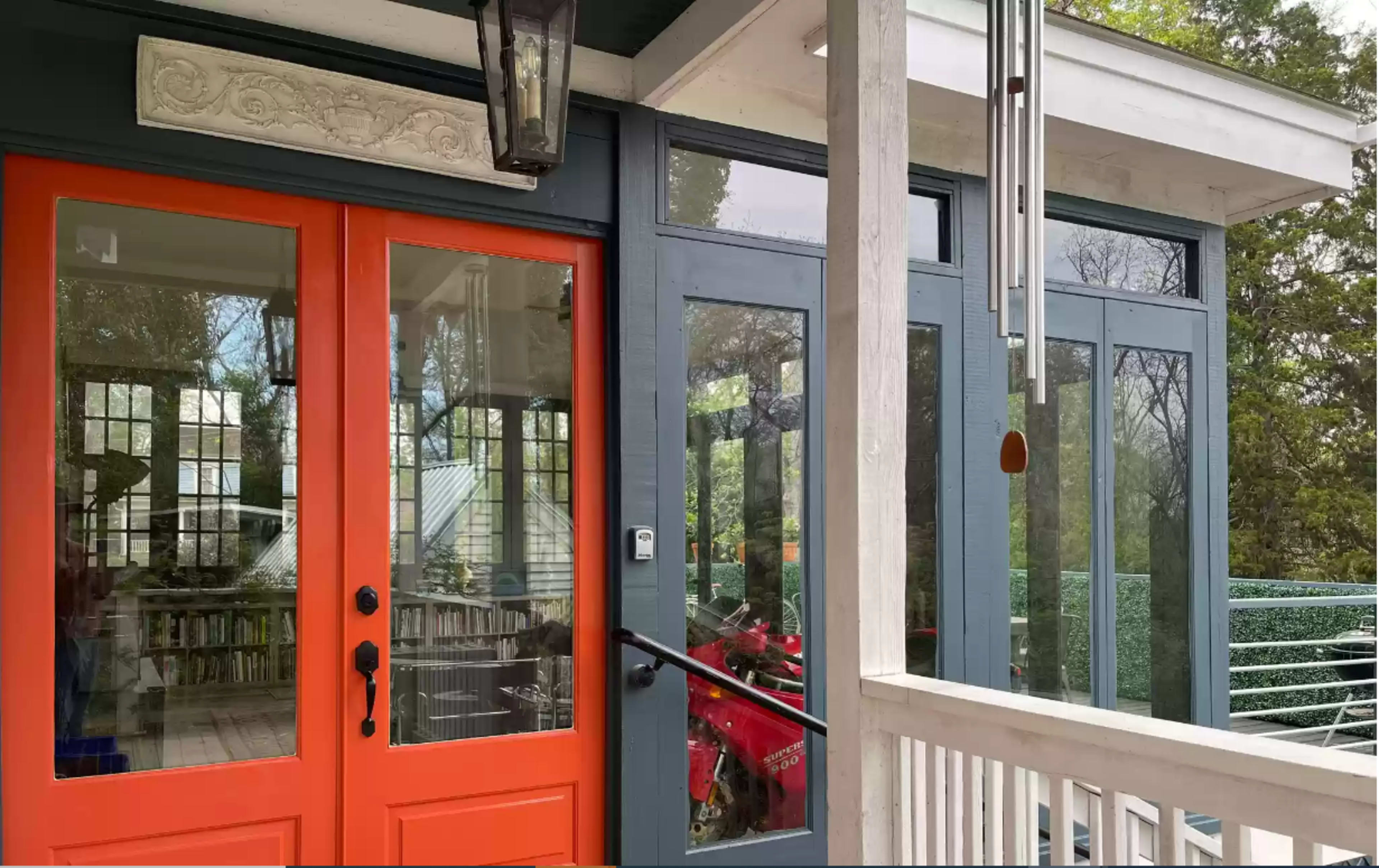 A house entrance with bright orange doors and large glass windows, showcasing a blend of modern and classic architectural elements.