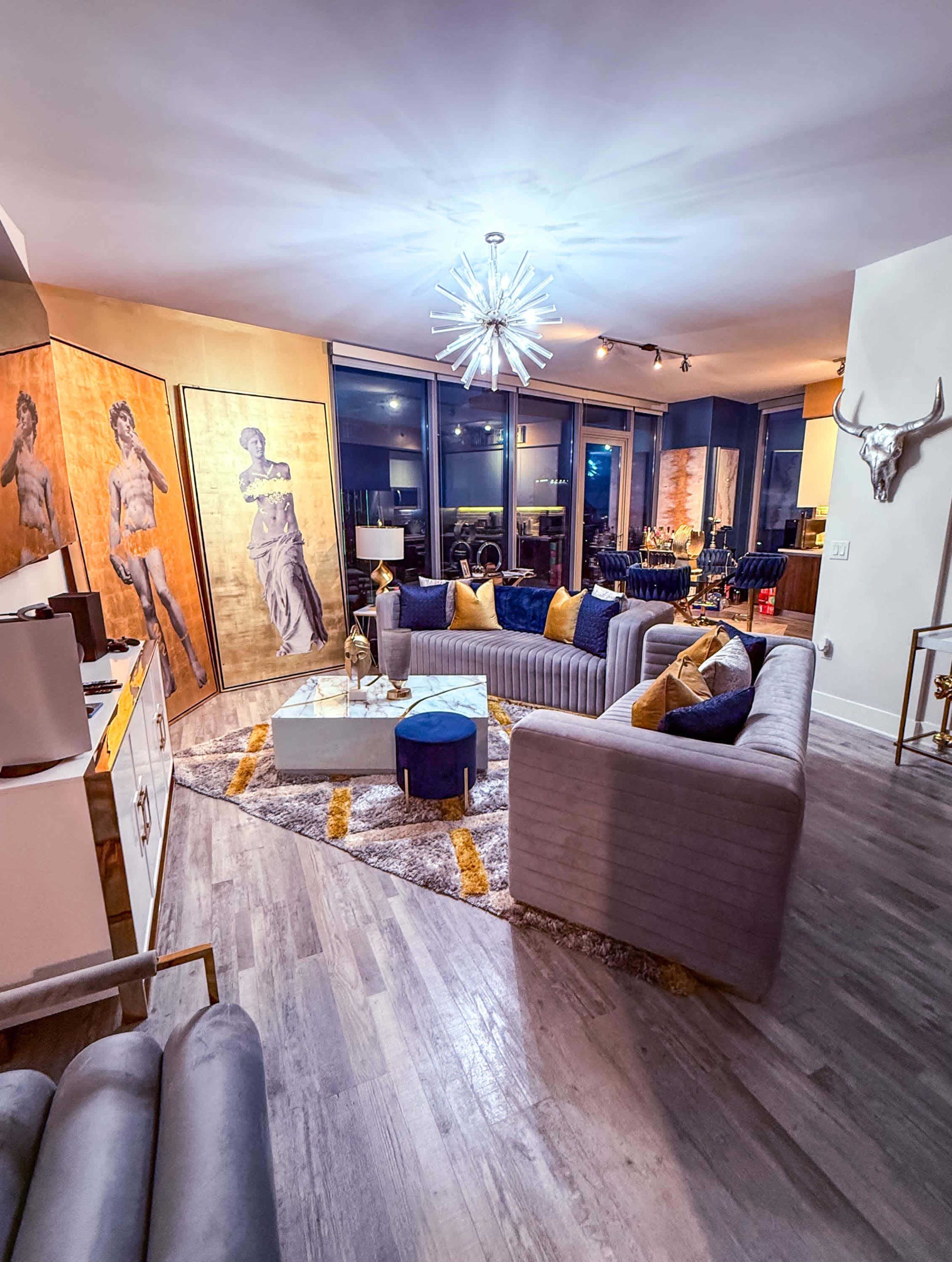 A modern living room features a circular gray sofa, decorative artwork on the walls, and a central glass coffee table.