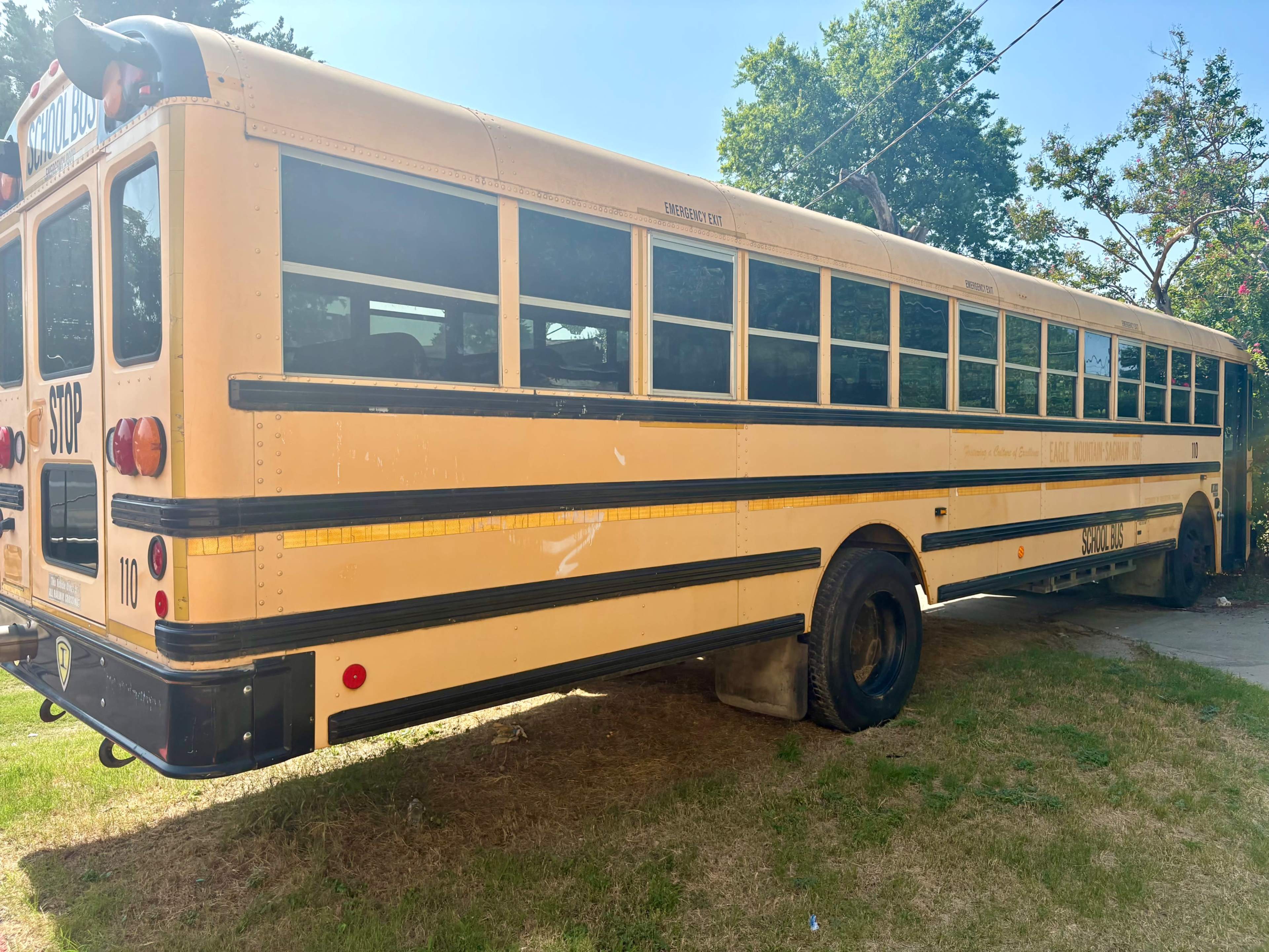A yellow school bus is parked on a grassy area beside a road.