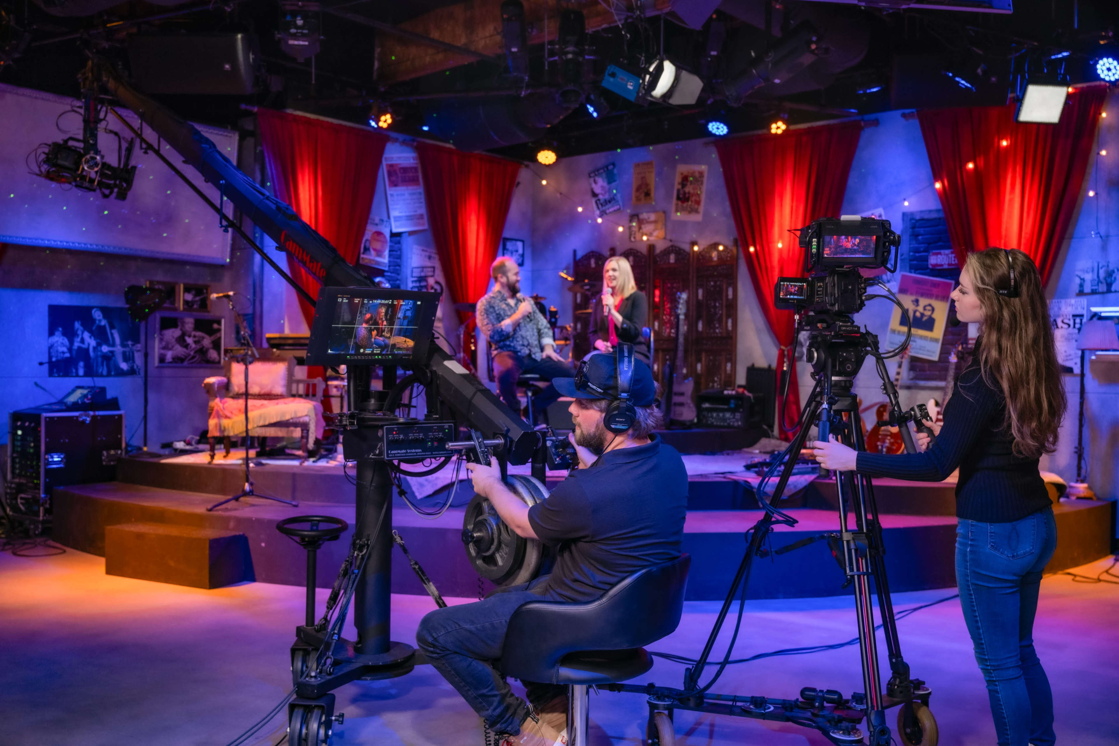 A television studio is set up for a live performance, featuring cameras, lighting equipment, and a band performing on stage.
