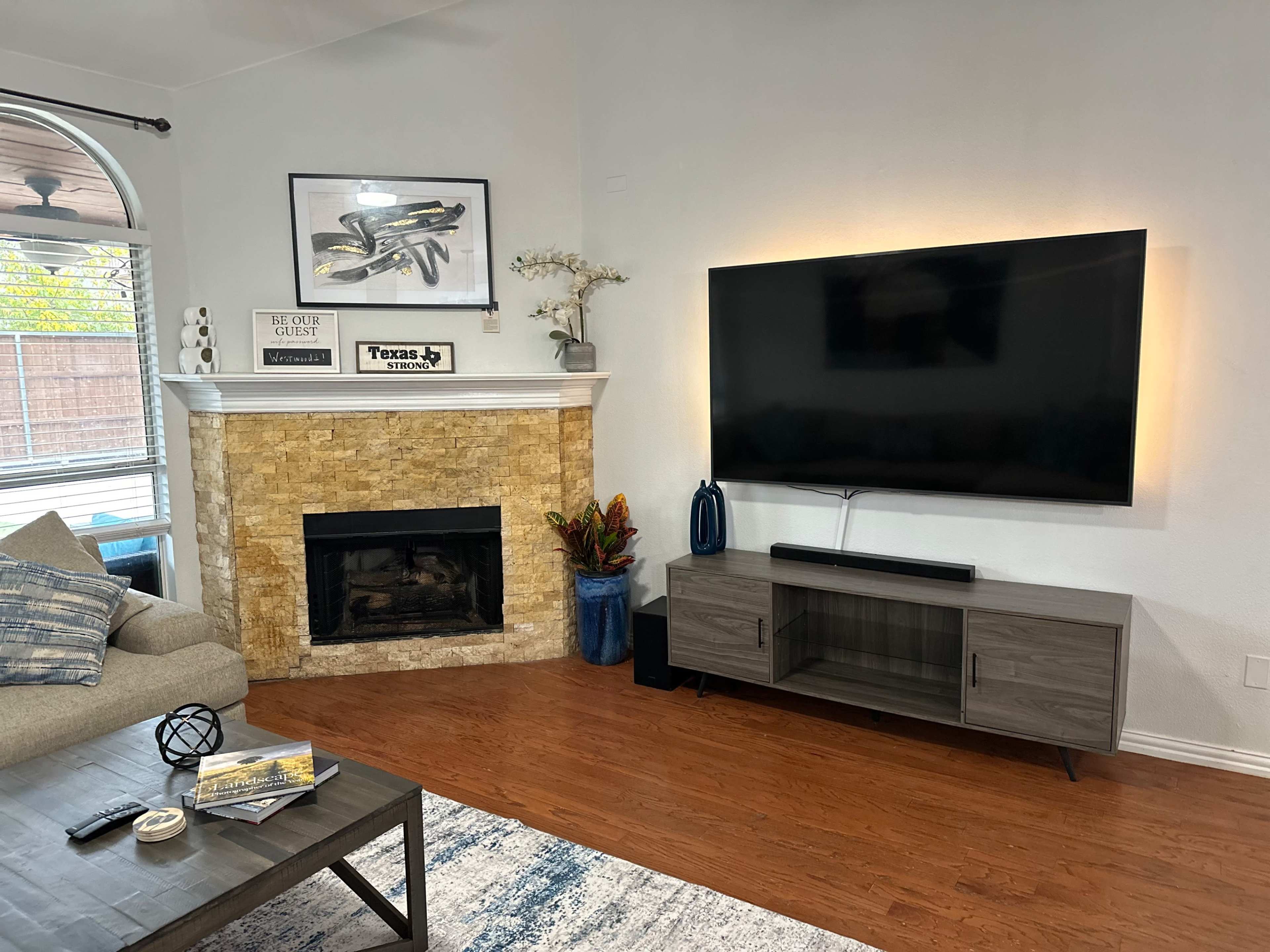 A living room featuring a stone fireplace, a mounted television, and a coffee table with decor items.