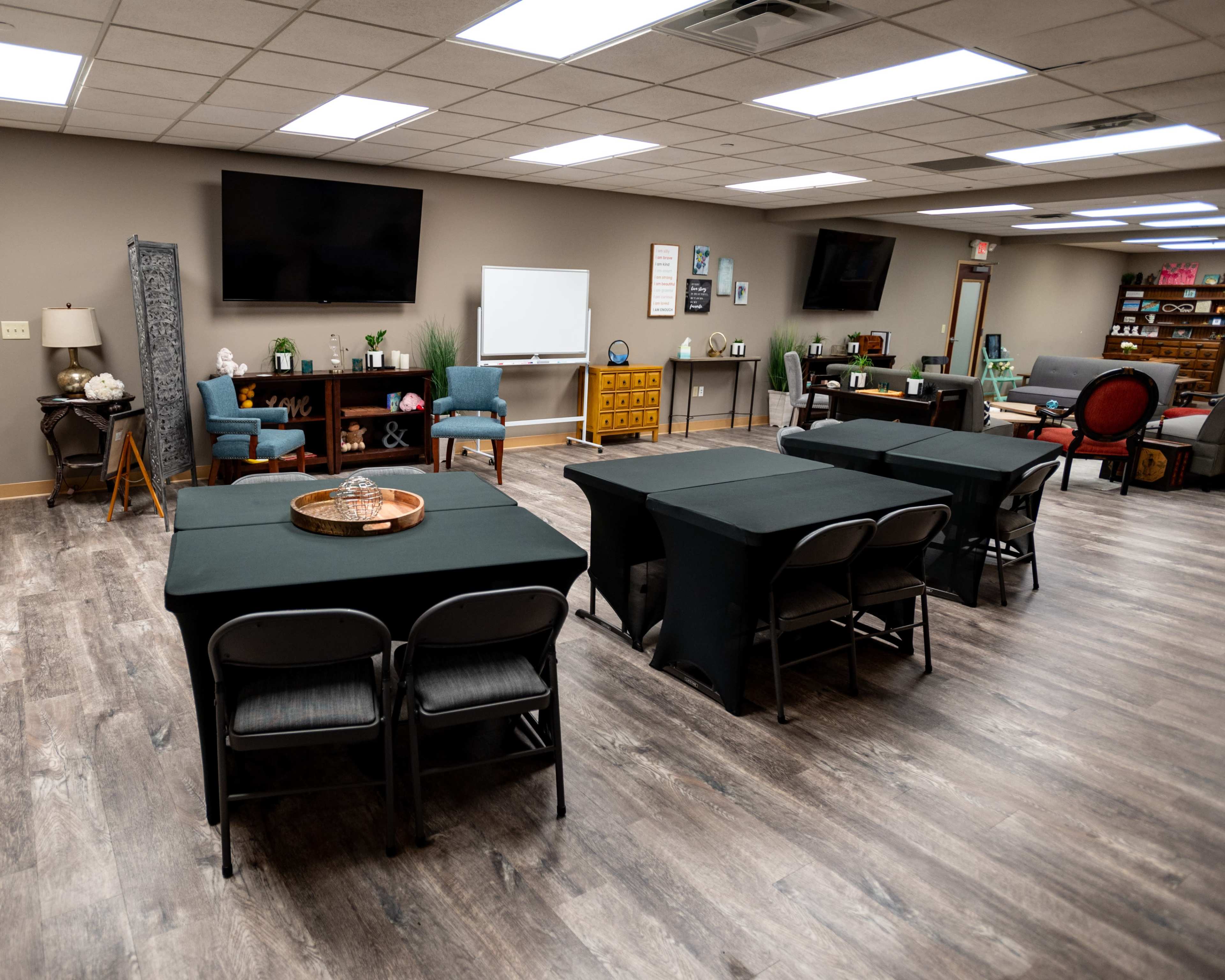 A spacious meeting room with multiple tables covered in black cloth, arranged alongside blue chairs and a whiteboard against the walls.