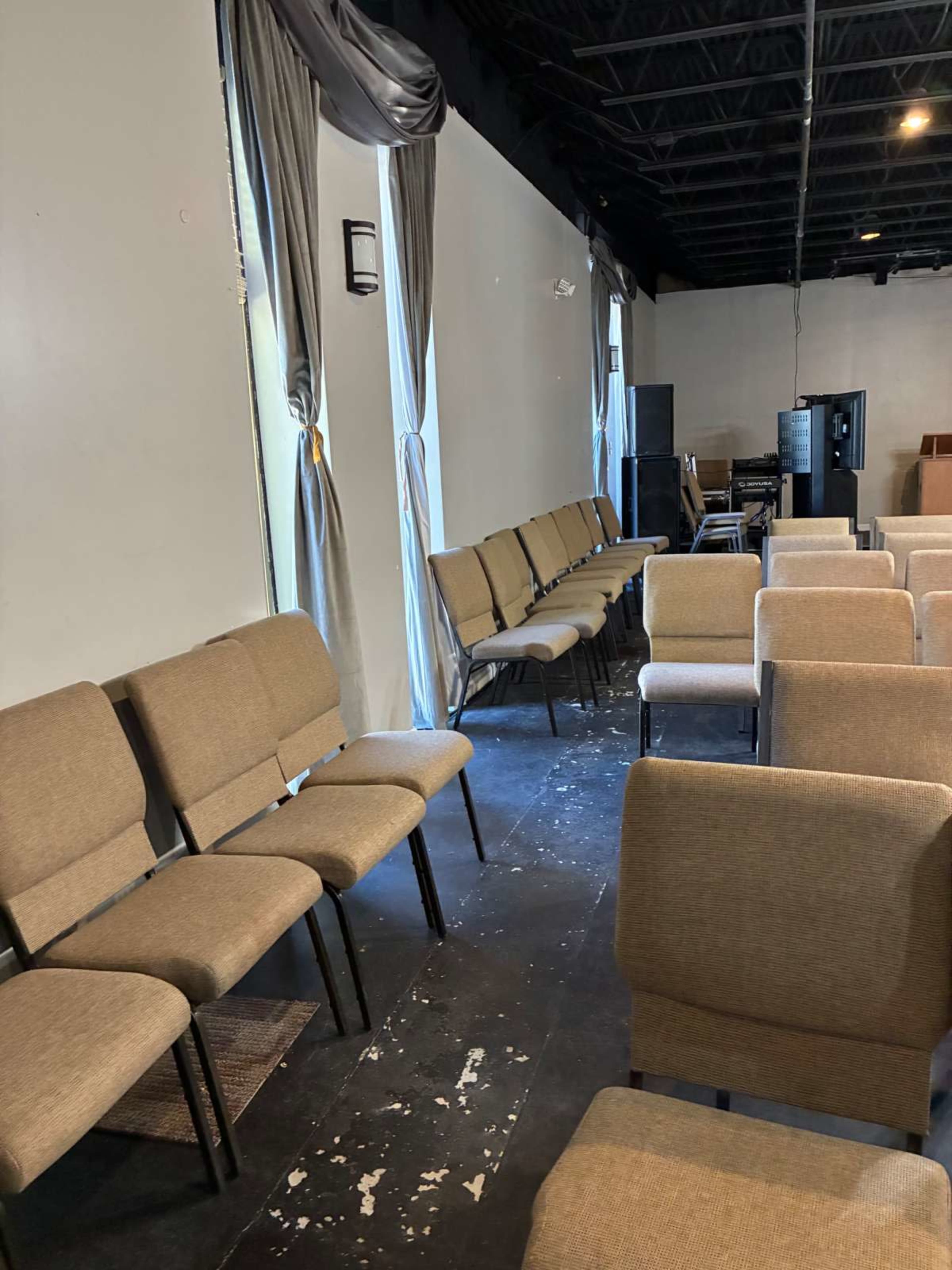The image shows rows of empty fabric-covered chairs arranged in a room with gray curtains and a dark floor.