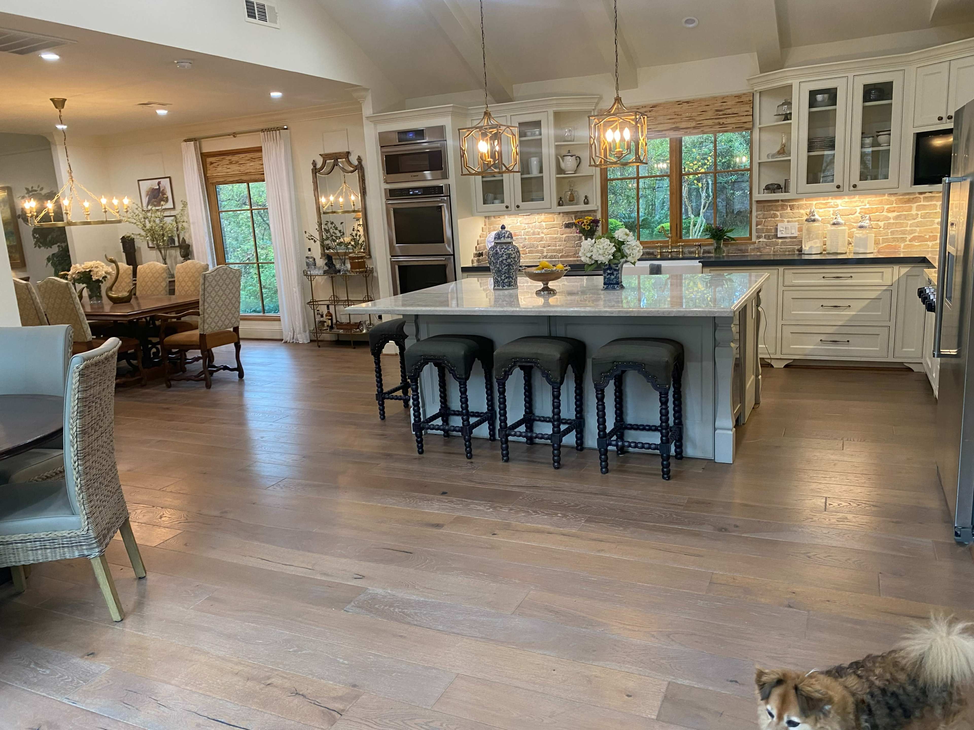 The image shows a spacious kitchen and dining area with a large island featuring bar stools, cabinets, and a dining table surrounded by chairs.