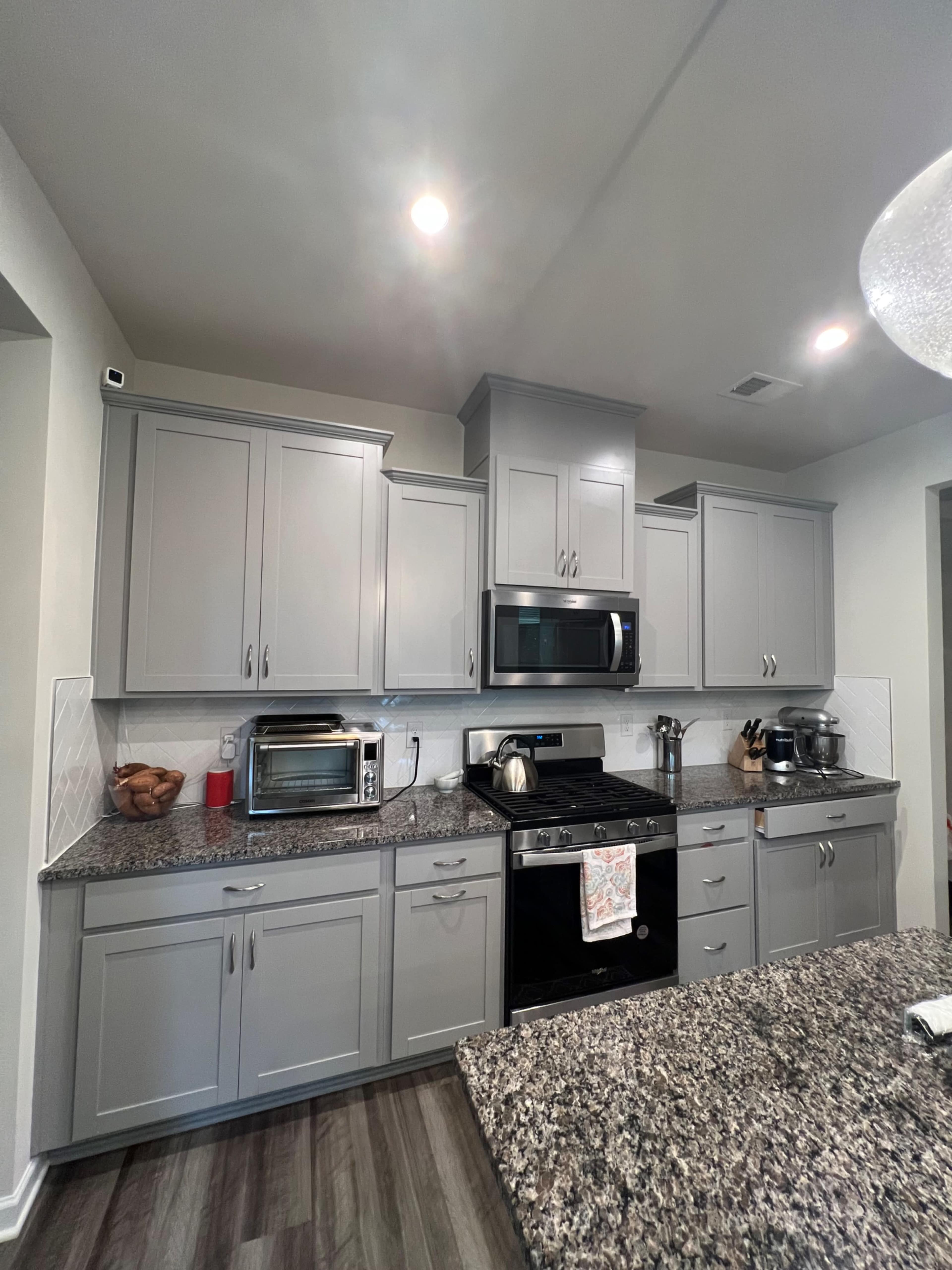 The image shows a modern kitchen with gray cabinets, a black oven, stainless steel appliances, and a granite countertop.