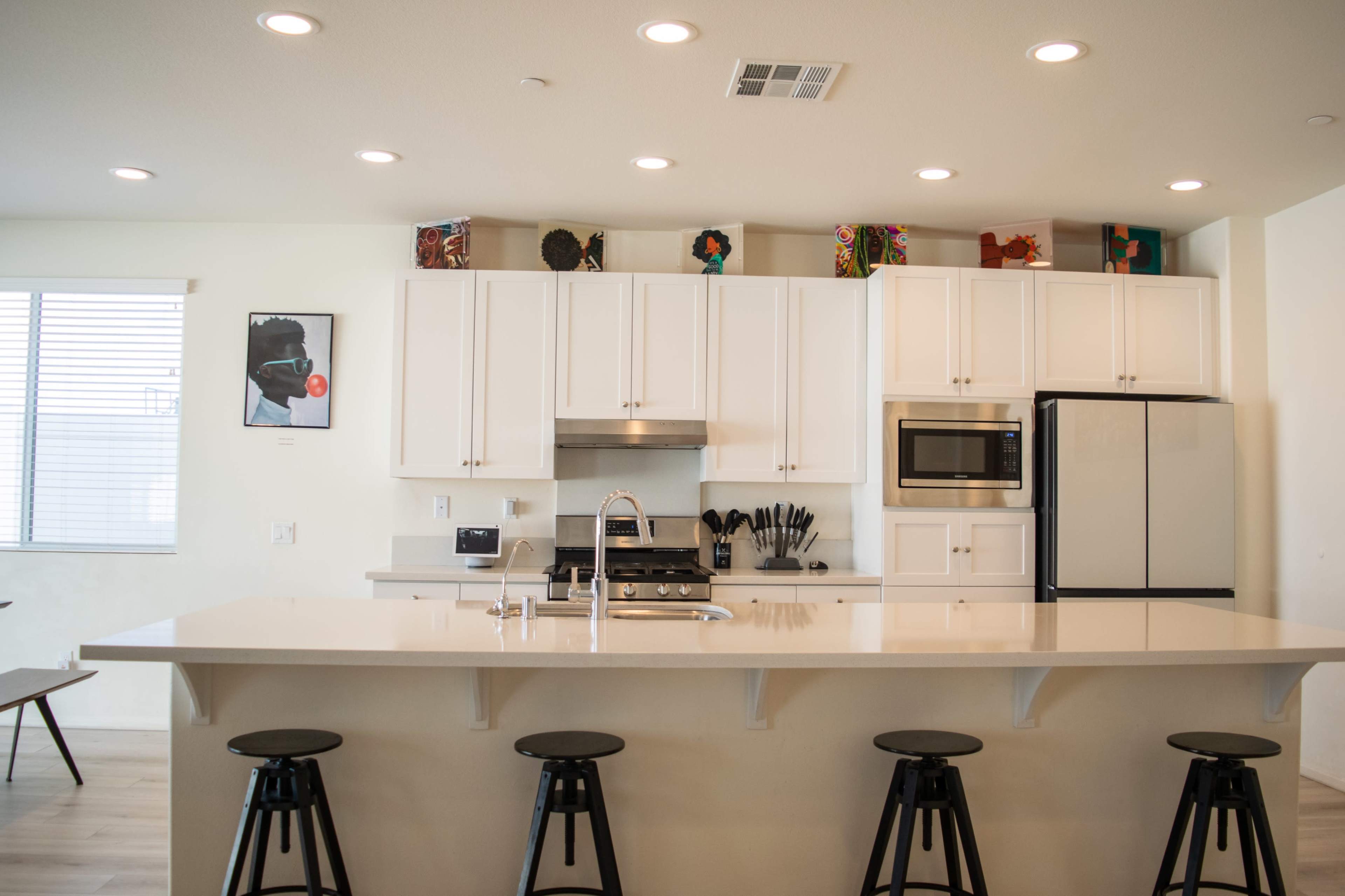 A modern kitchen with white cabinetry, a large island with bar stools, and stainless steel appliances.