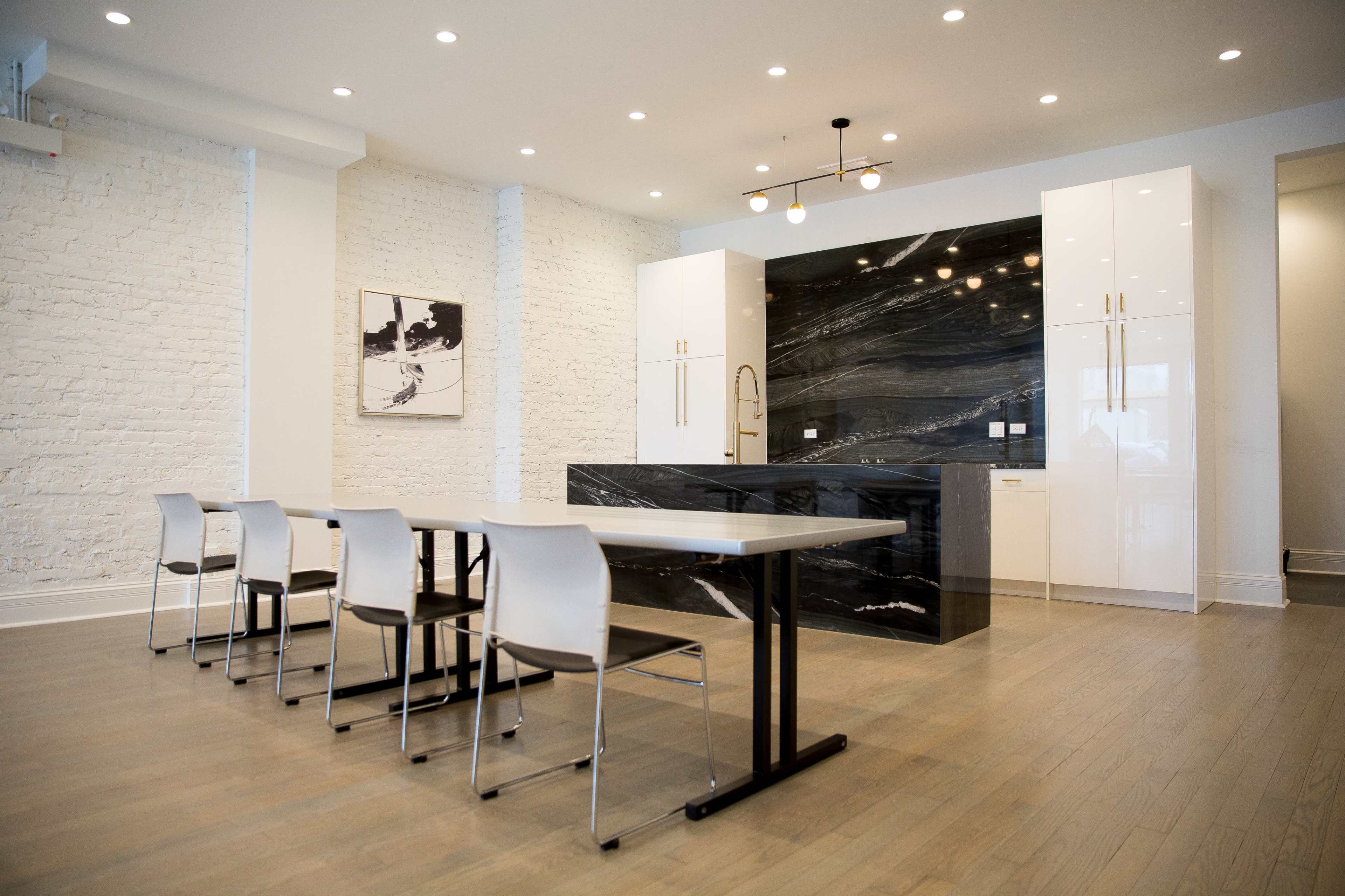 A modern kitchen features white brick walls, a dark stone backsplash, sleek cabinetry, and a dining table with metal chairs.
