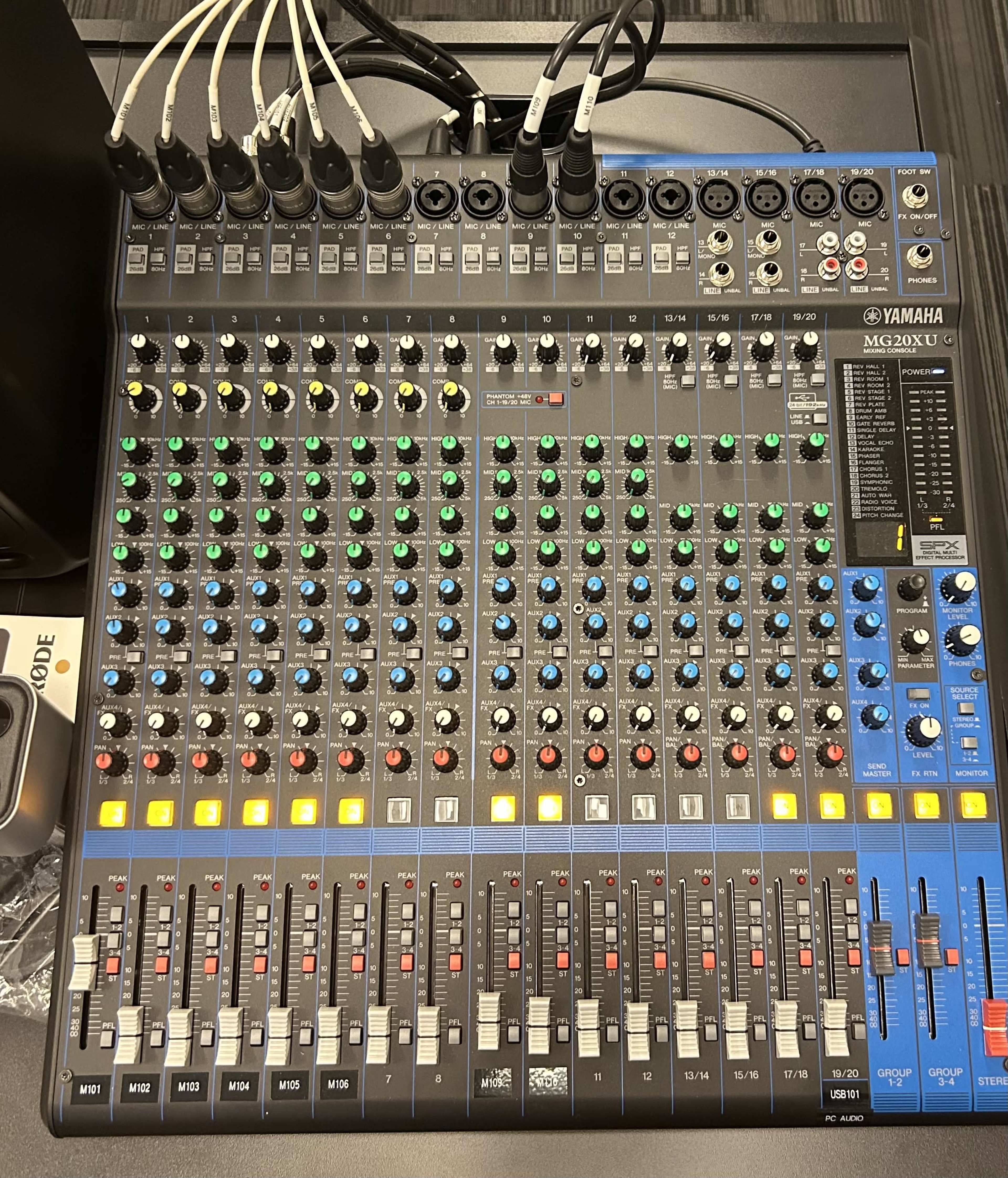 The image shows a Yamaha MG20XU audio mixing console with multiple faders, knobs, and inputs.