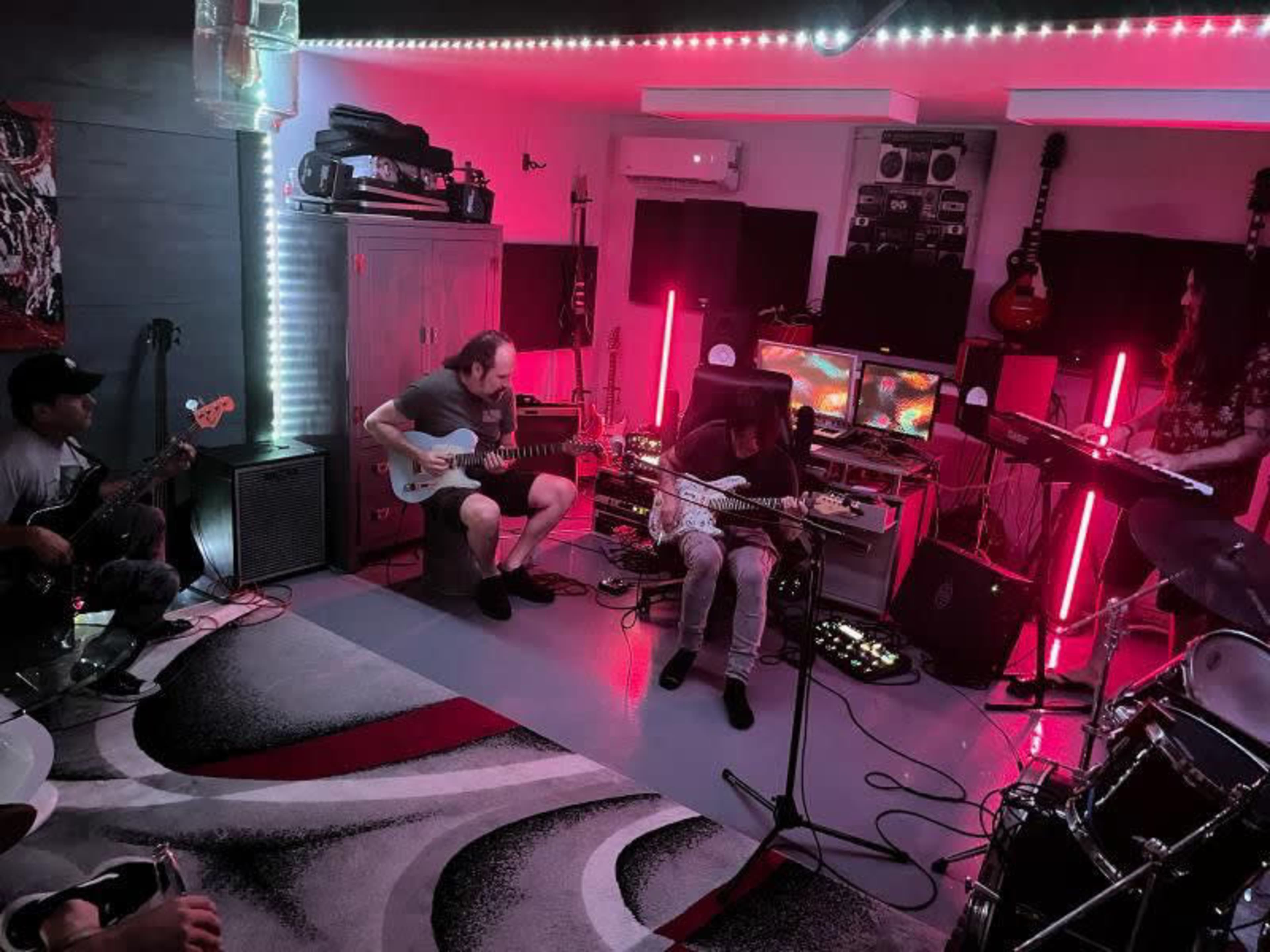 A group of musicians is playing instruments in a dimly lit rehearsal space with colorful LED lighting.