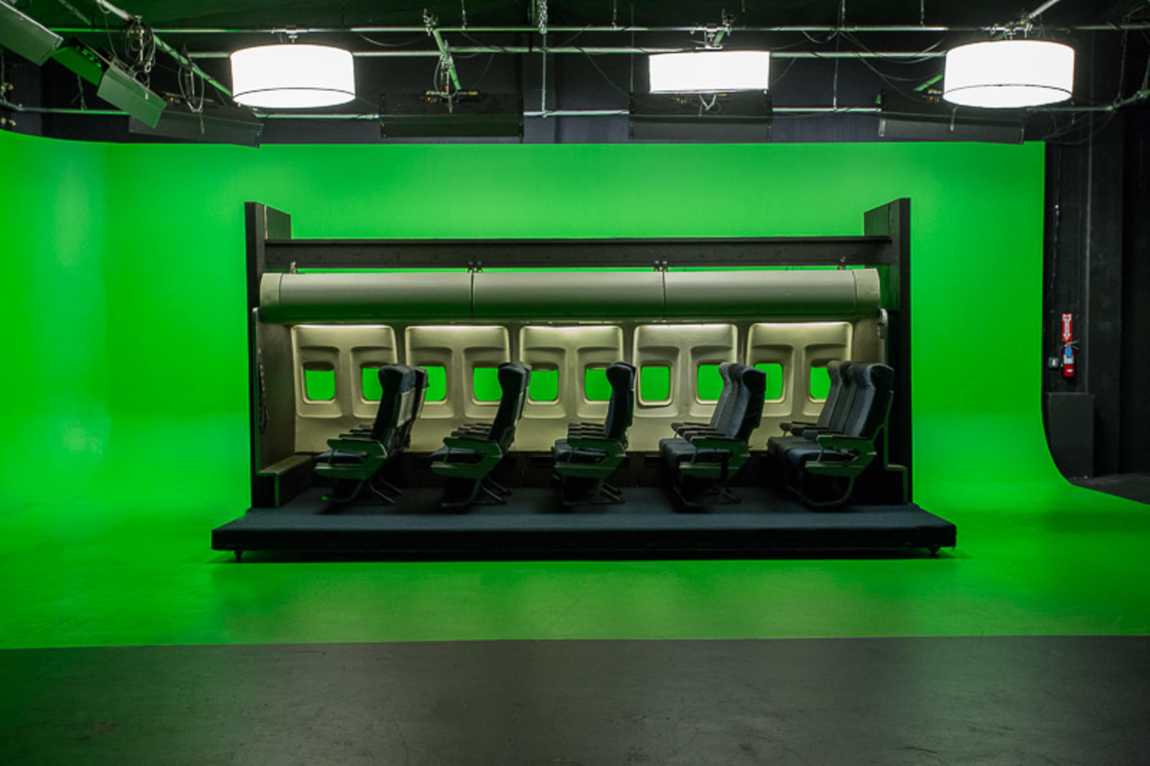 A row of airplane seats set against a bright green screen backdrop in a studio environment.